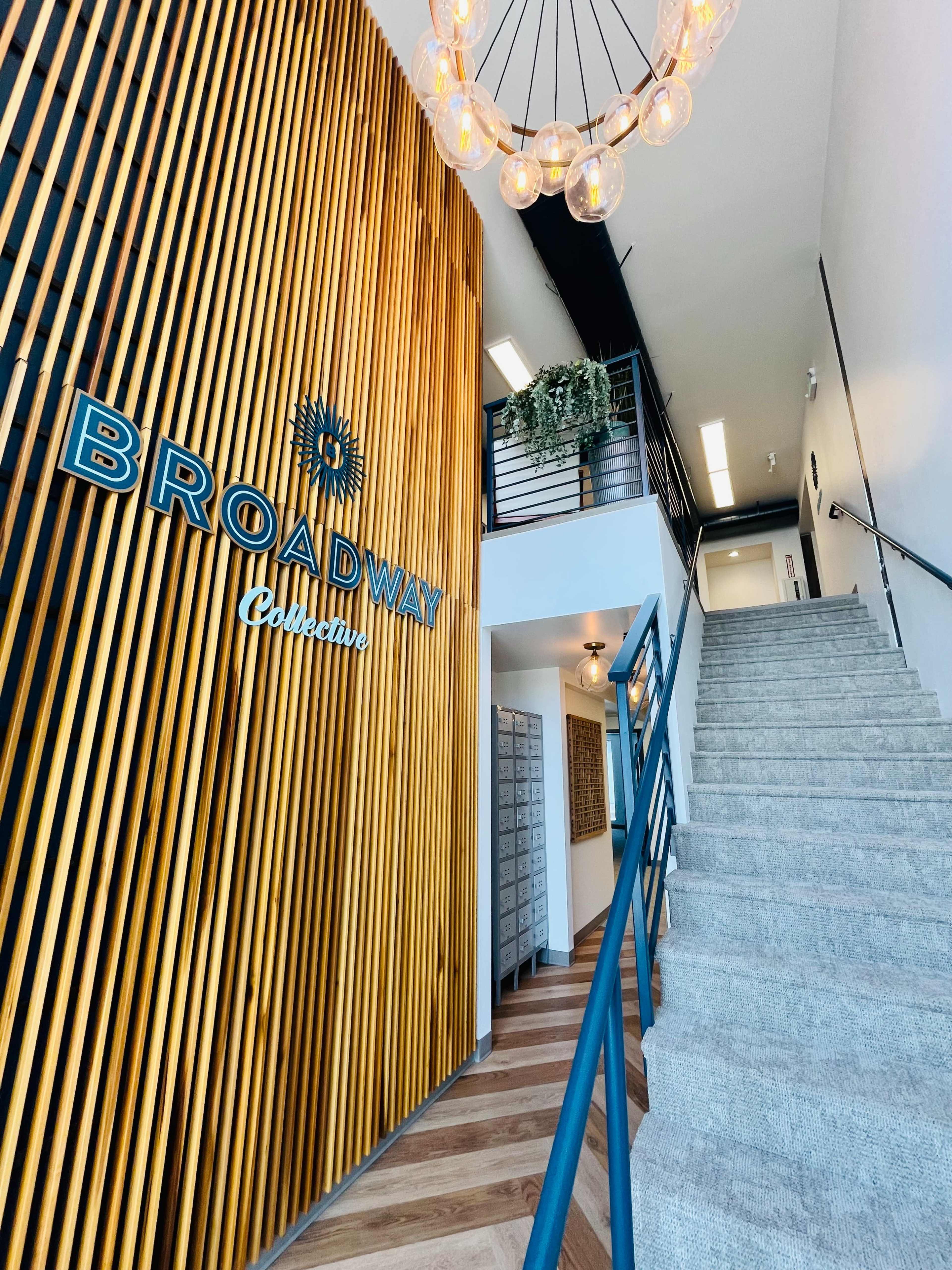 A stairway leading to an upper level with a wooden wall displaying the text "BROADWAY Collective" and a decorative light fixture overhead.