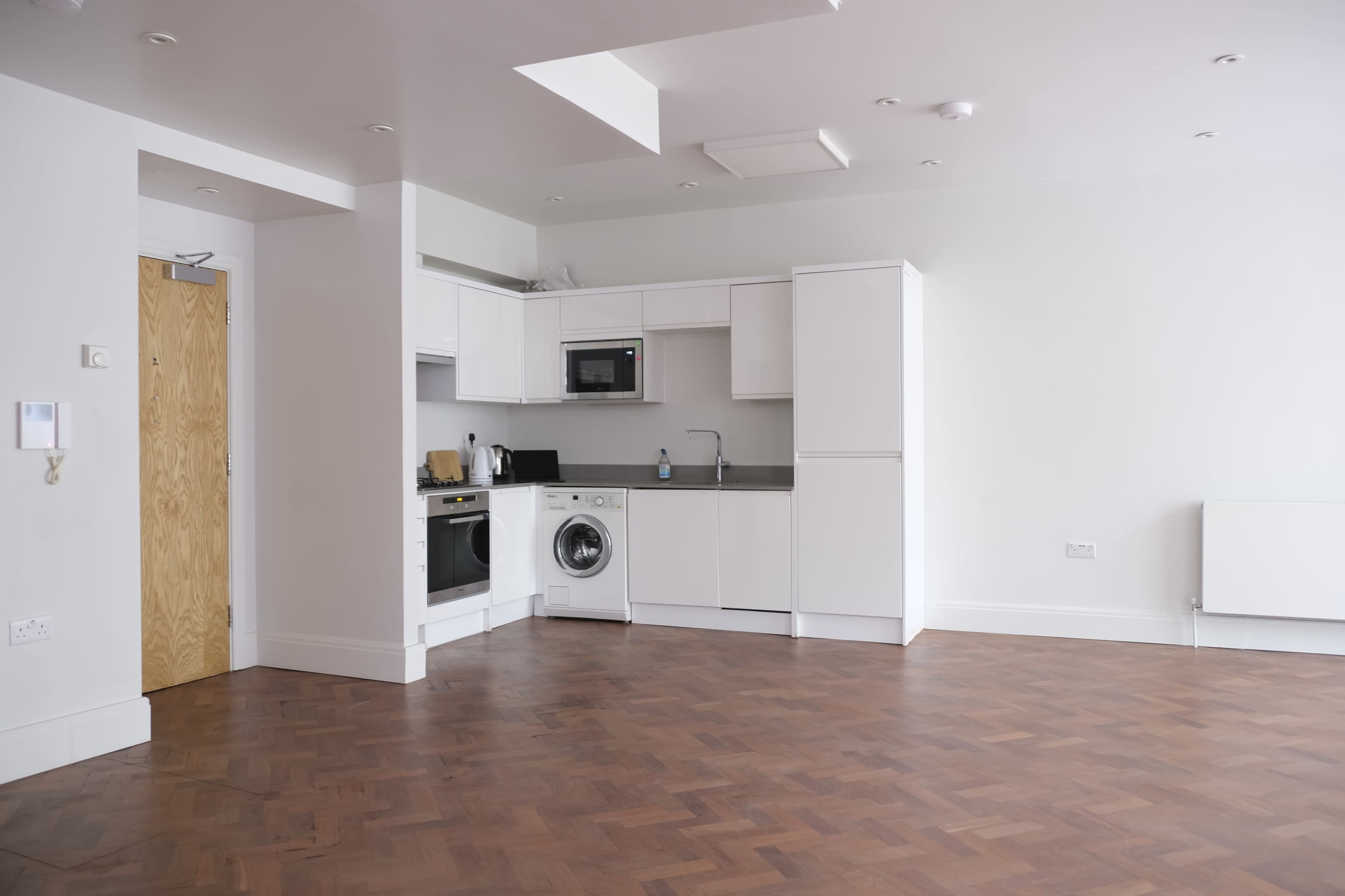 A modern kitchen area with white cabinets and appliances, featuring a washing machine and a wooden floor.
