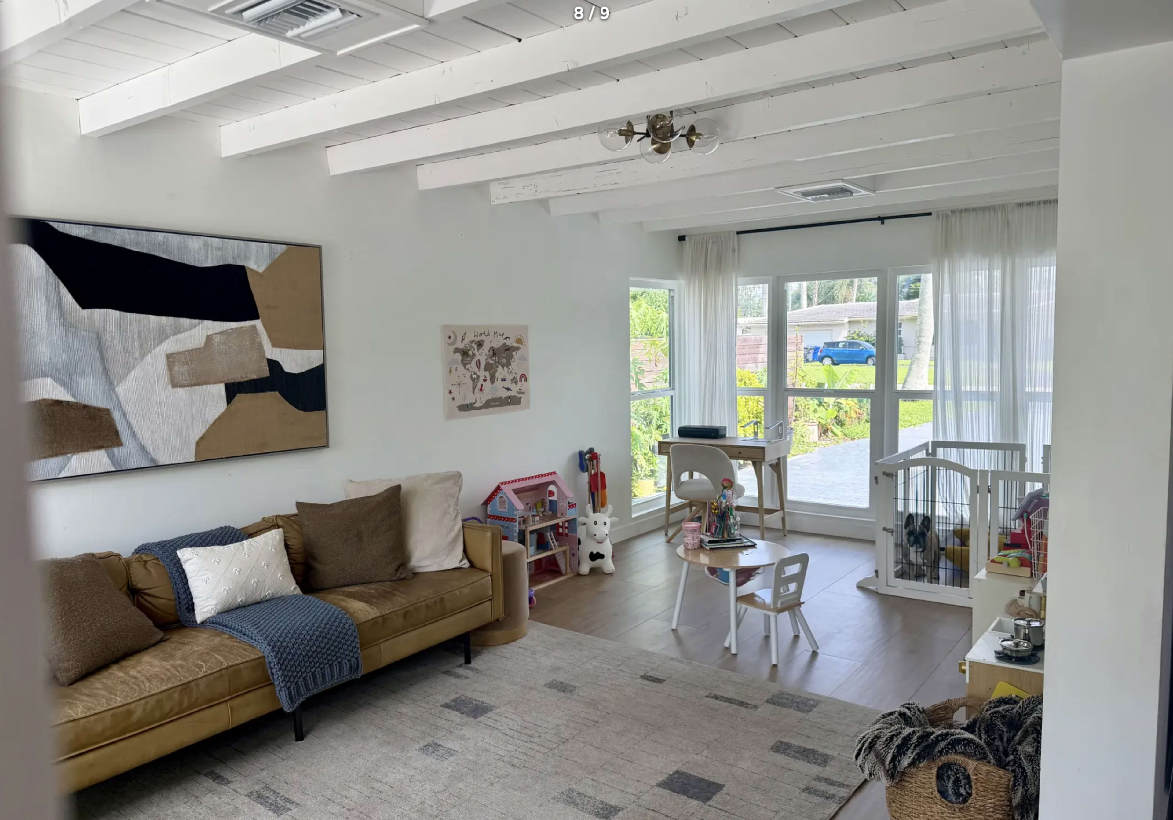 The image shows a cozy living room with a brown sofa, children's toys, and large windows letting in natural light.