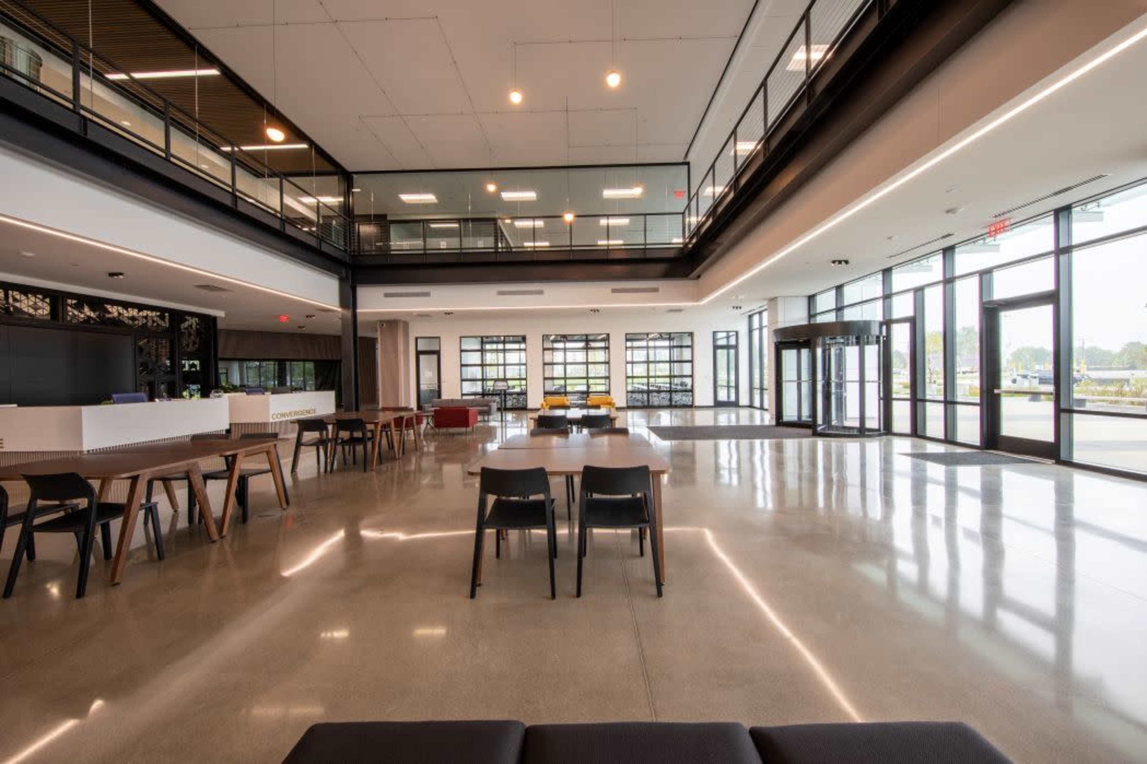 The image shows a modern, open lobby area with polished concrete floors, multiple seating arrangements, and large glass windows allowing natural light to flood the space.