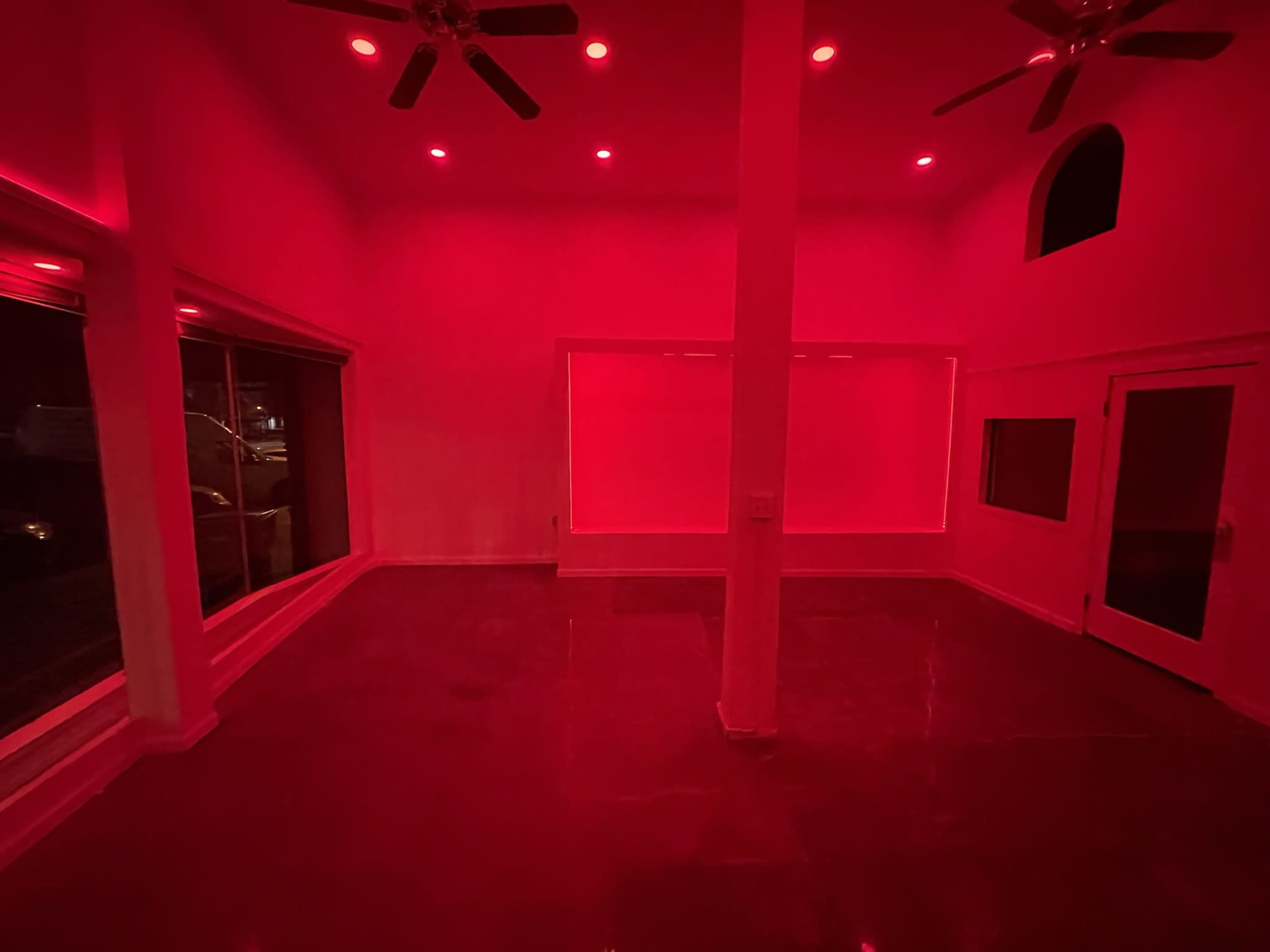 The room features red lighting and polished concrete floors with large windows and multiple ceiling fans.