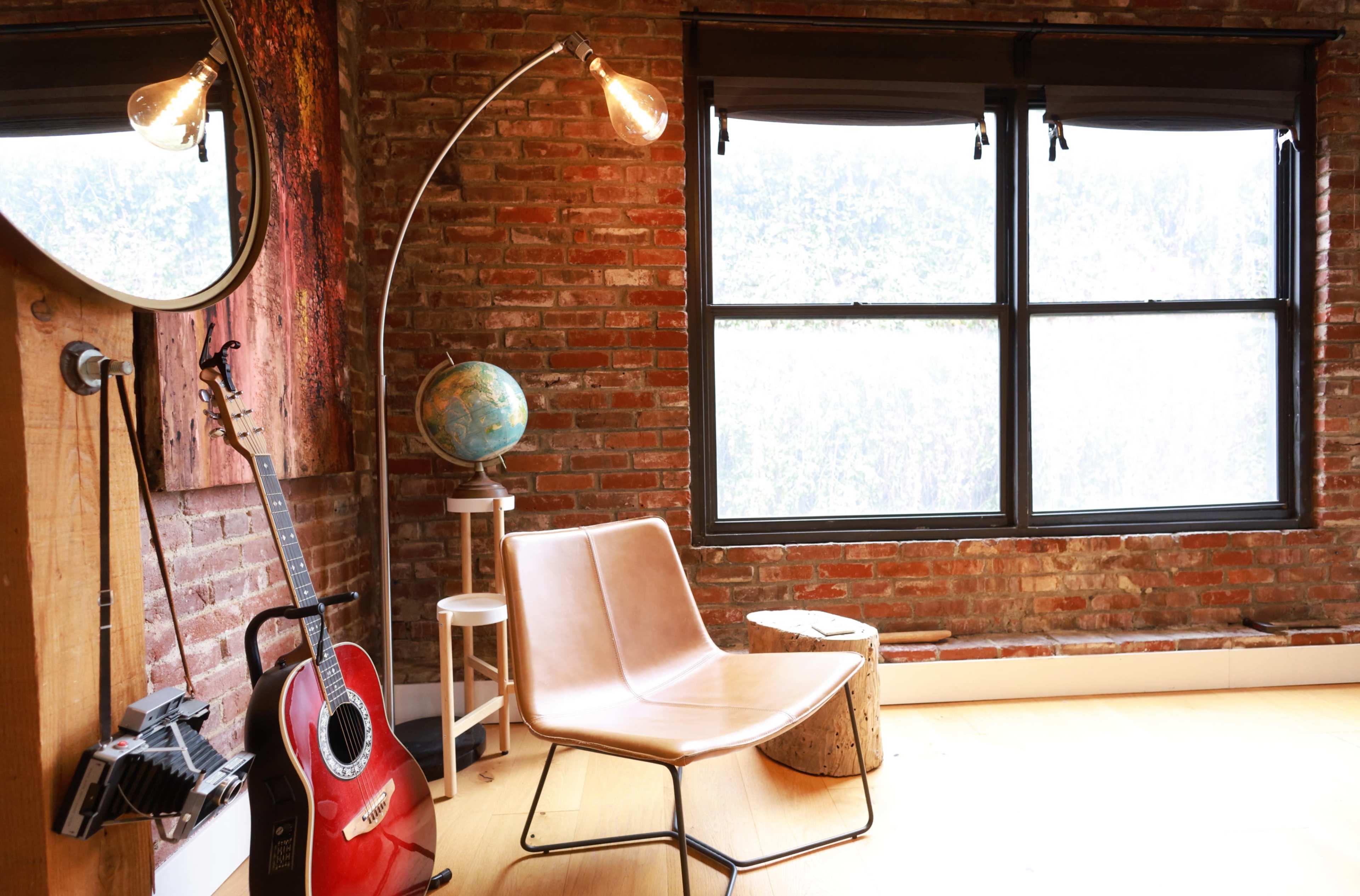 The scene features a cozy corner of a room with a leather chair, a guitar, a globe, and a large window with brick walls.