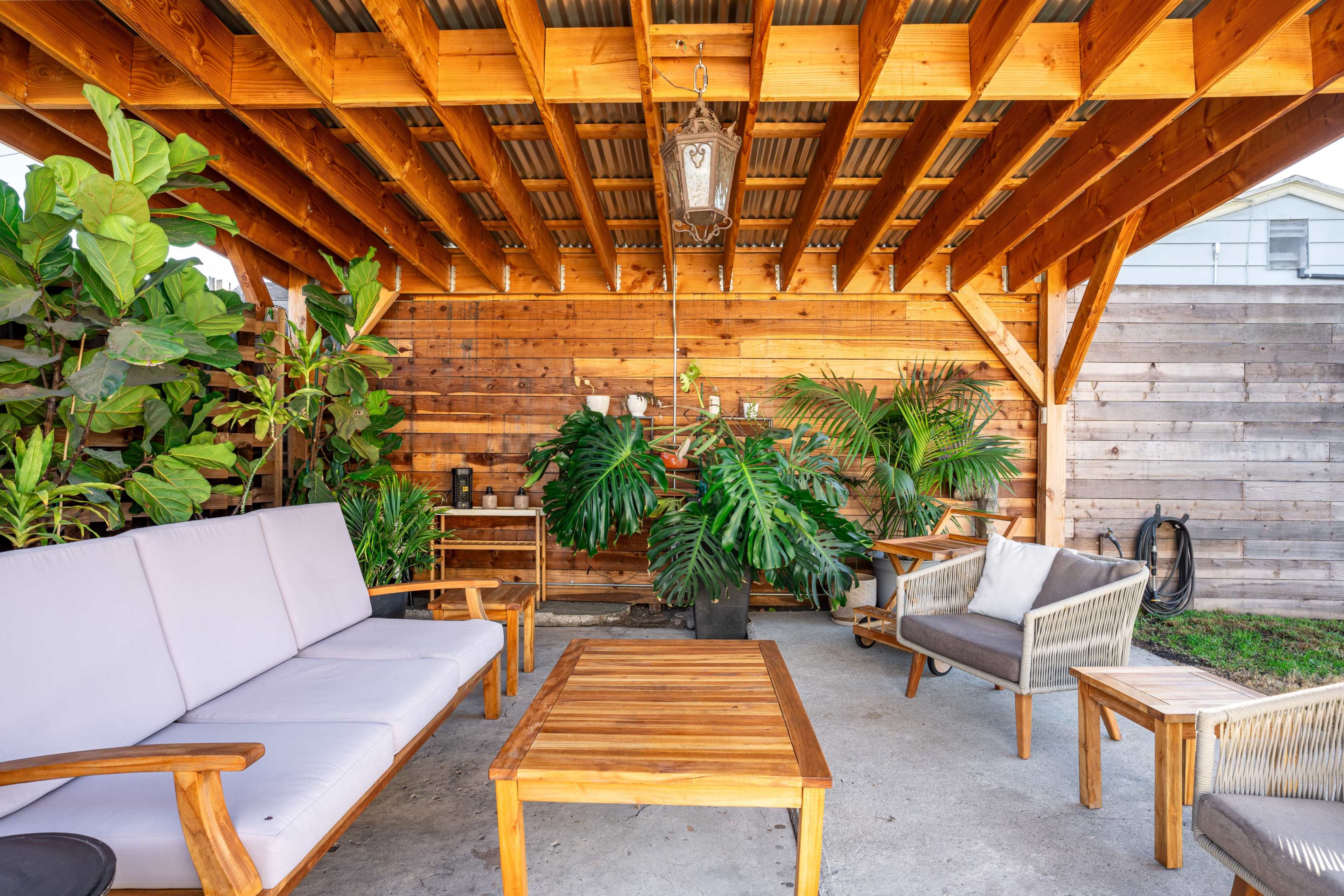 A wooden patio shelter features seating arrangements and various indoor plants in pots.