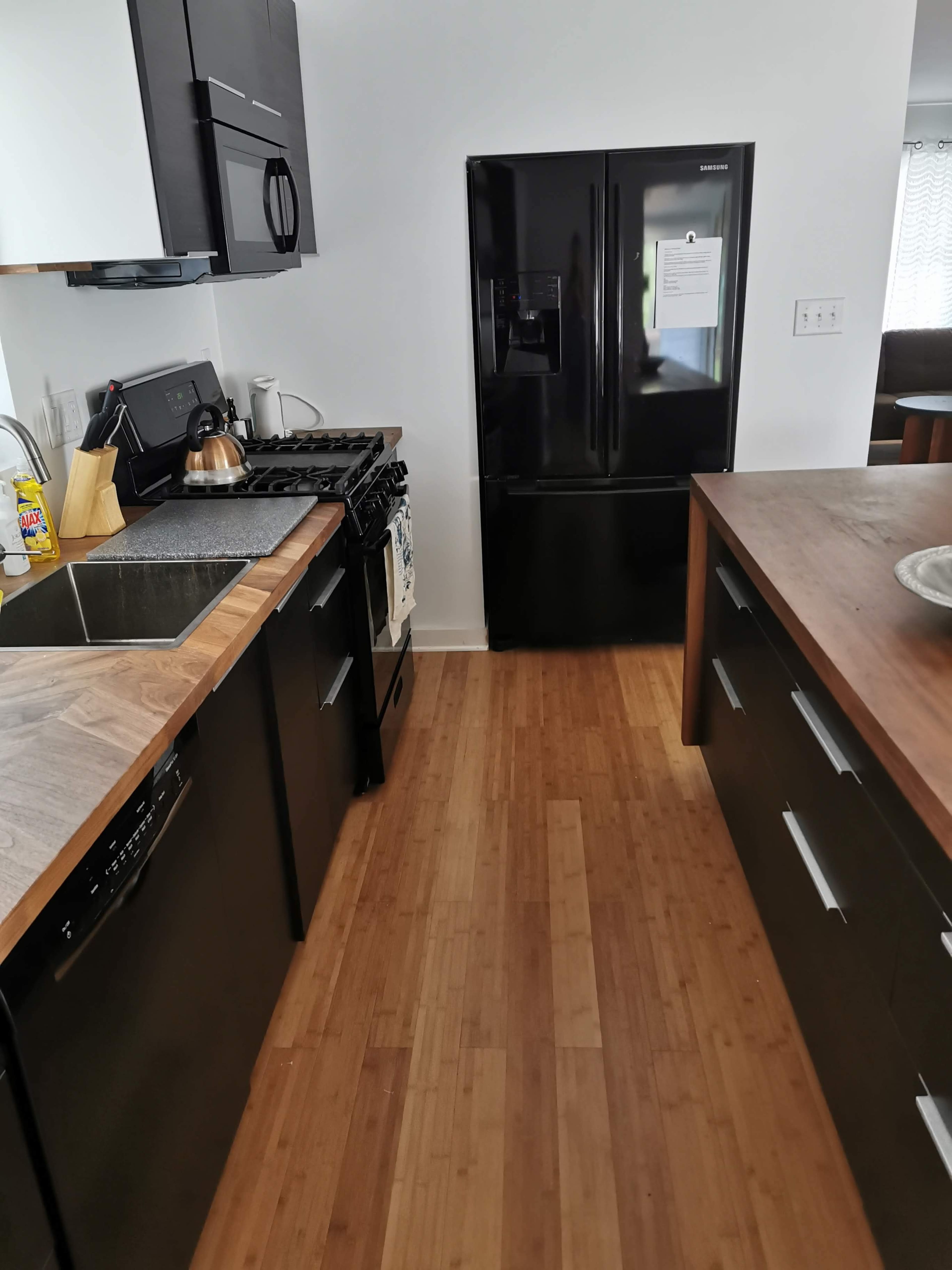 The kitchen features dark cabinetry, a stainless steel sink, a gas stove, and a black refrigerator, all arranged along a bamboo floor.