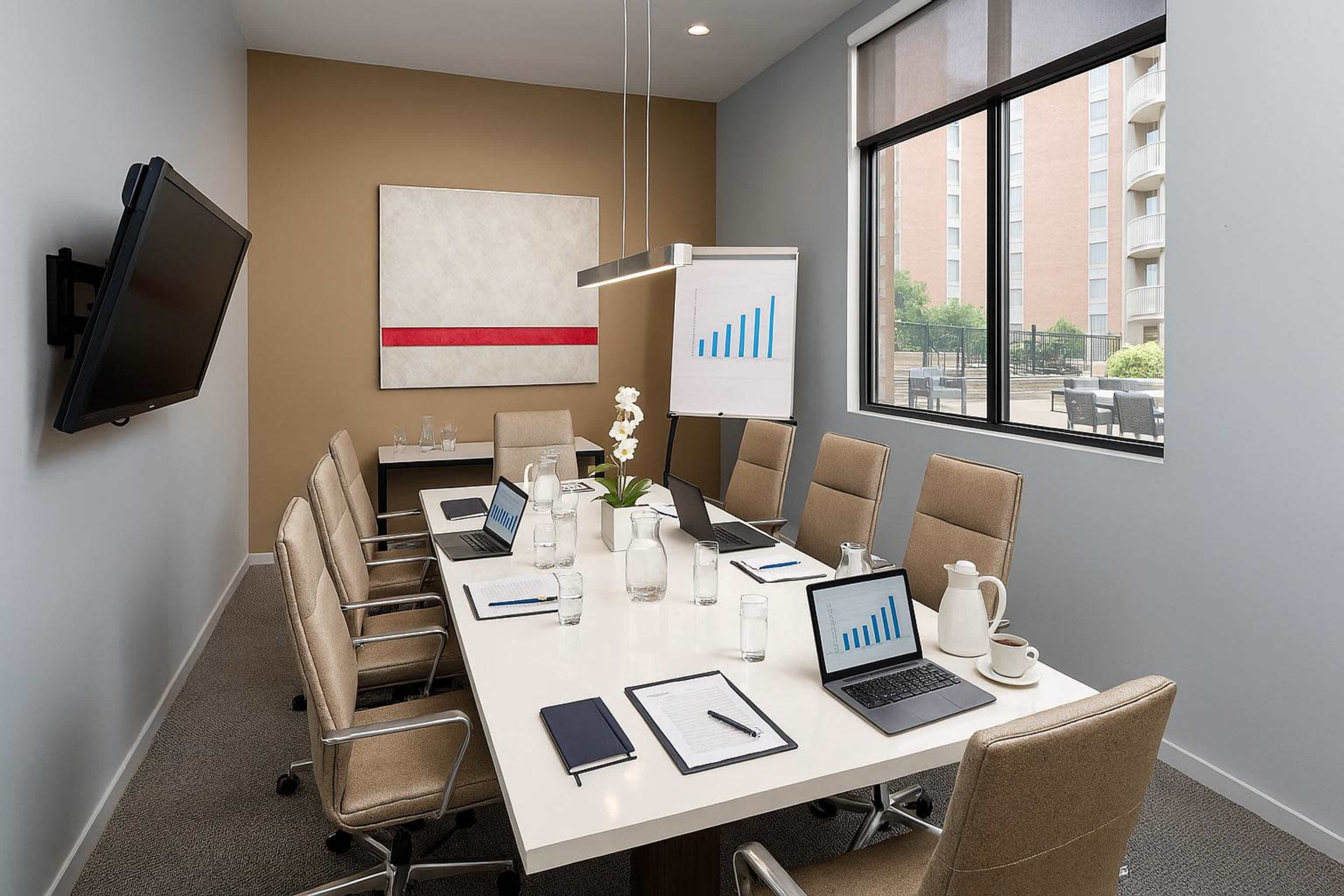 A modern conference room features a long table with chairs, a monitor on the wall, and a presentation chart displaying a rising graph.