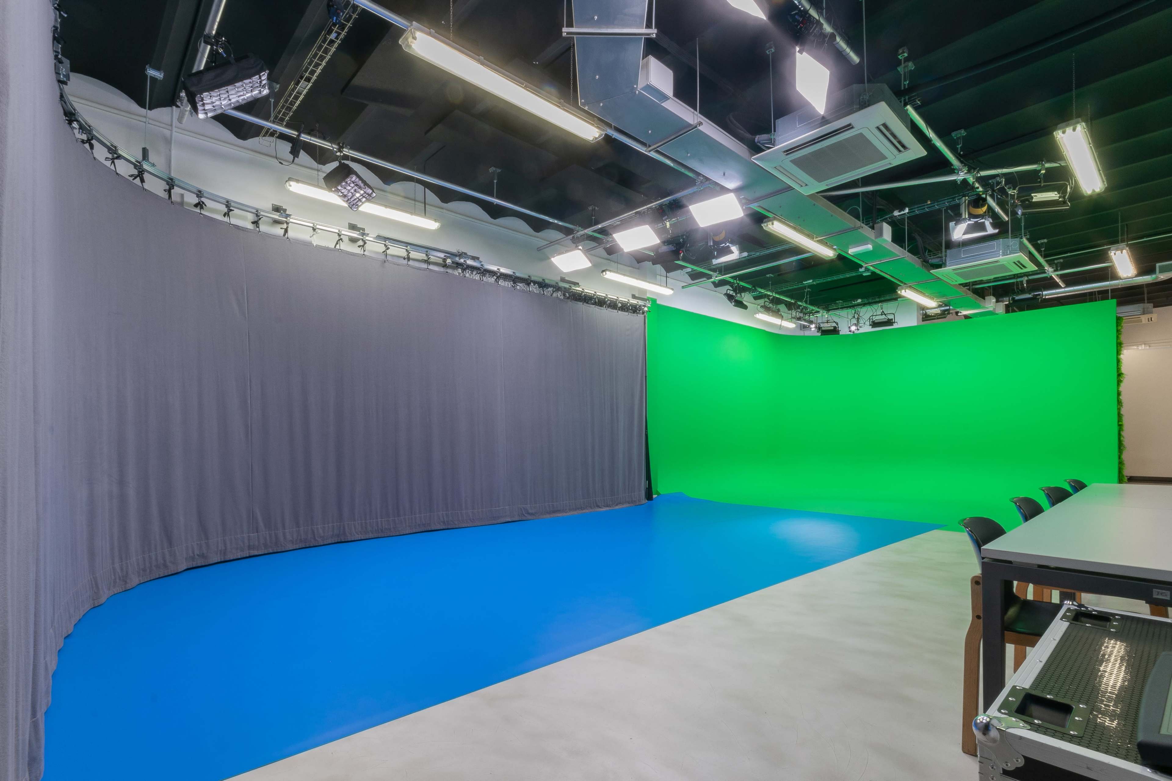 A studio with a green backdrop, gray drapes, and a blue floor, equipped with overhead lights.