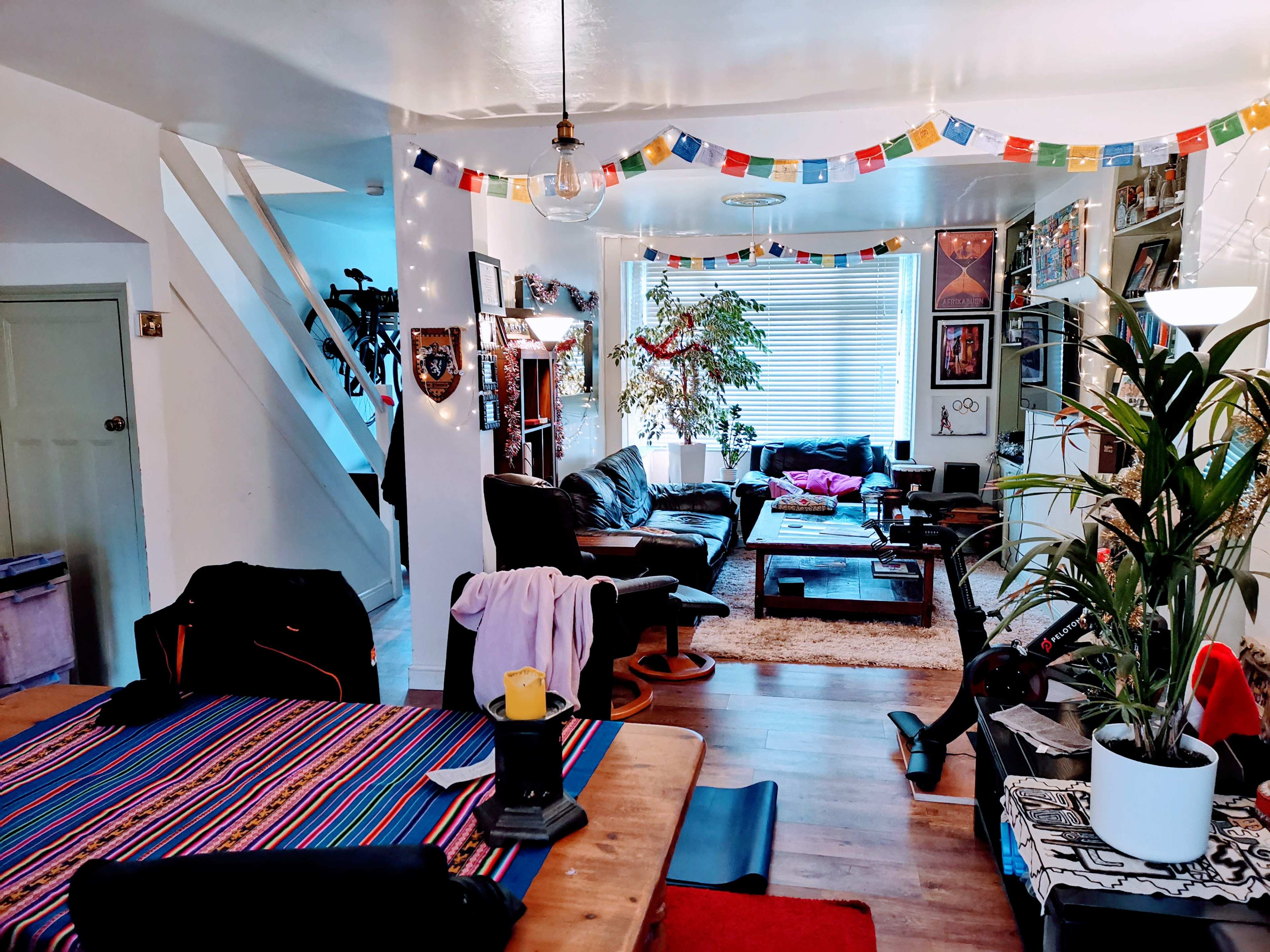 A cozy living room and dining area featuring a patterned tablecloth, a large plant, and colorful decorations strung across the ceiling.