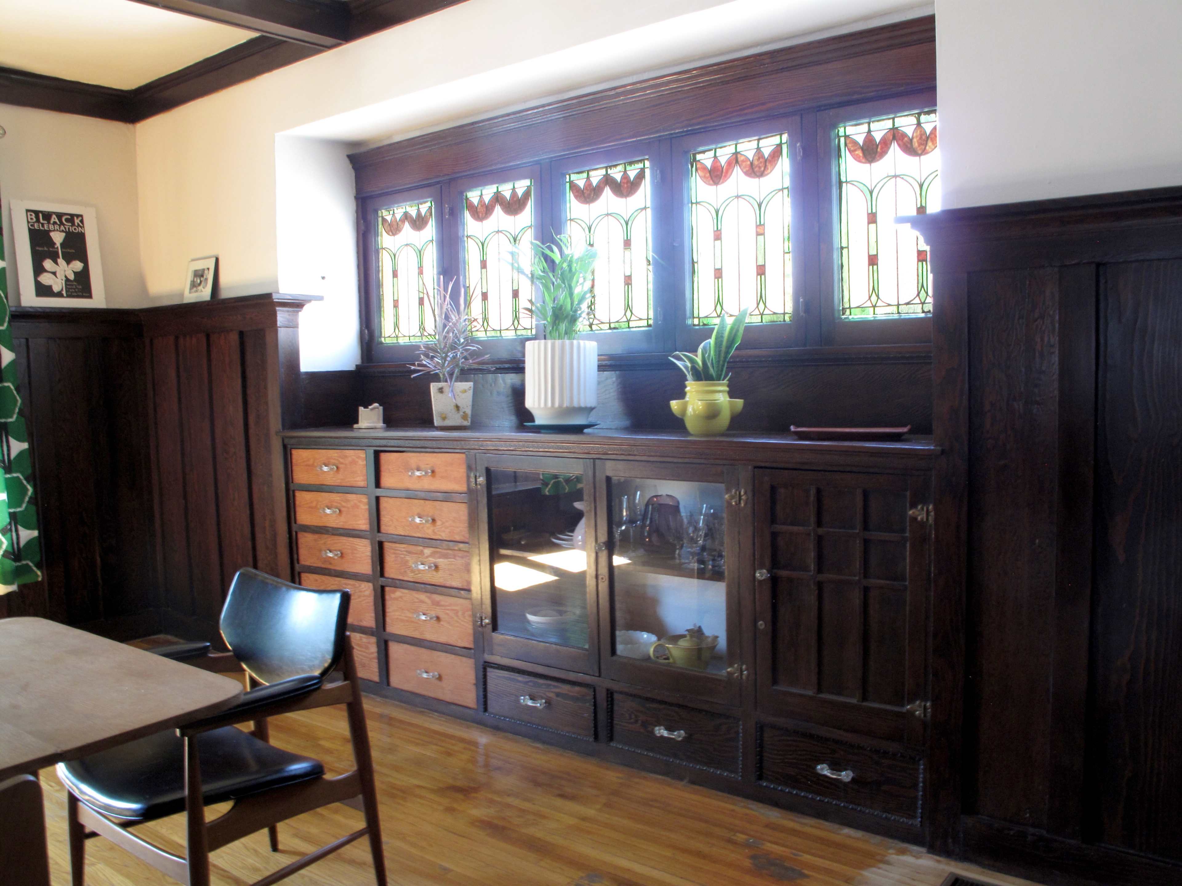 A wooden sideboard with multiple drawers and glass-front cabinets, positioned beneath a row of stained glass windows.