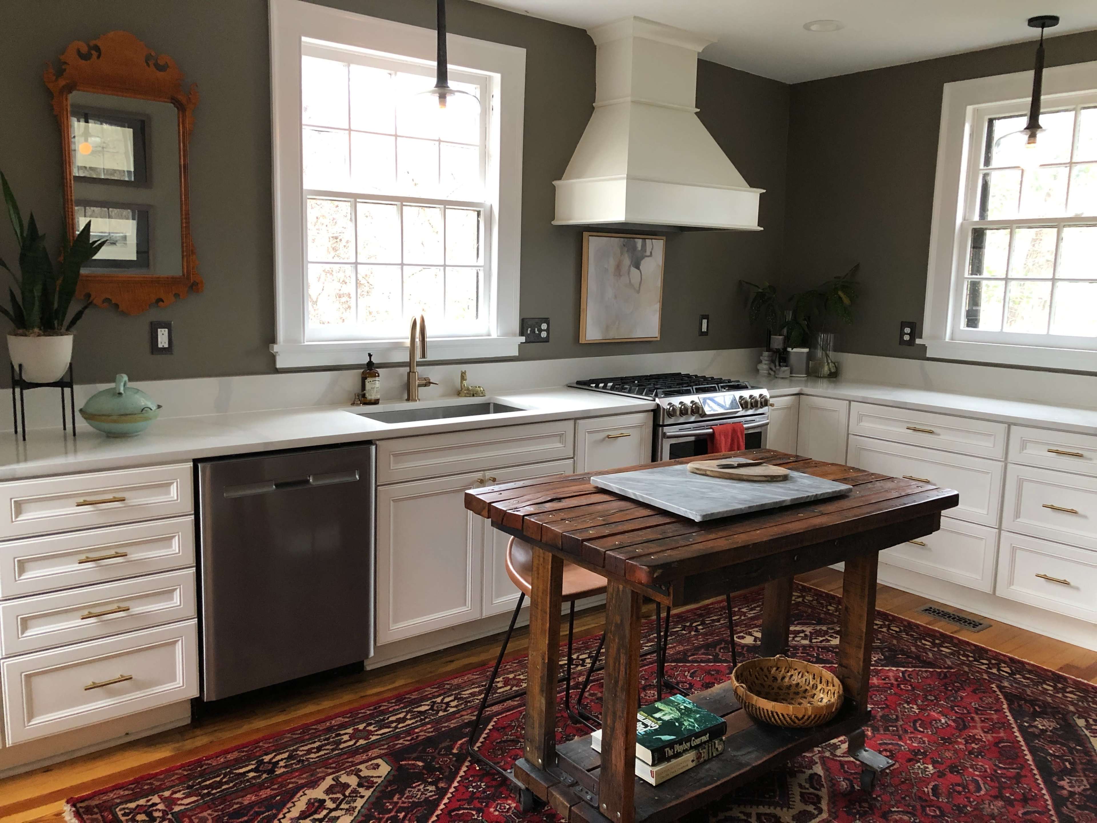A modern kitchen features white cabinetry, stainless steel appliances, and a wooden island on a patterned rug.