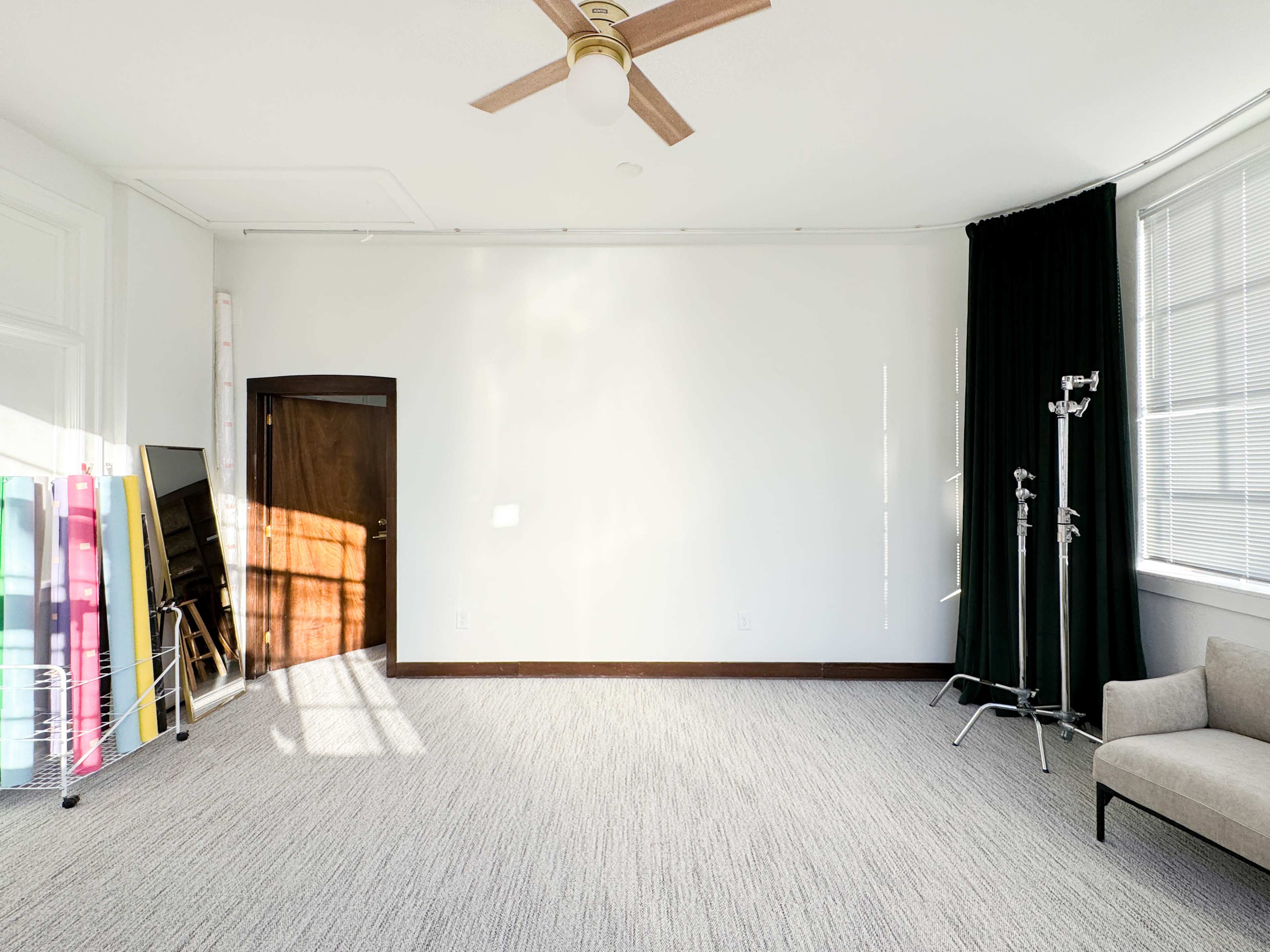 The image shows an empty room with a fan on the ceiling, a grey sofa, and various colored backdrops leaning against the wall.