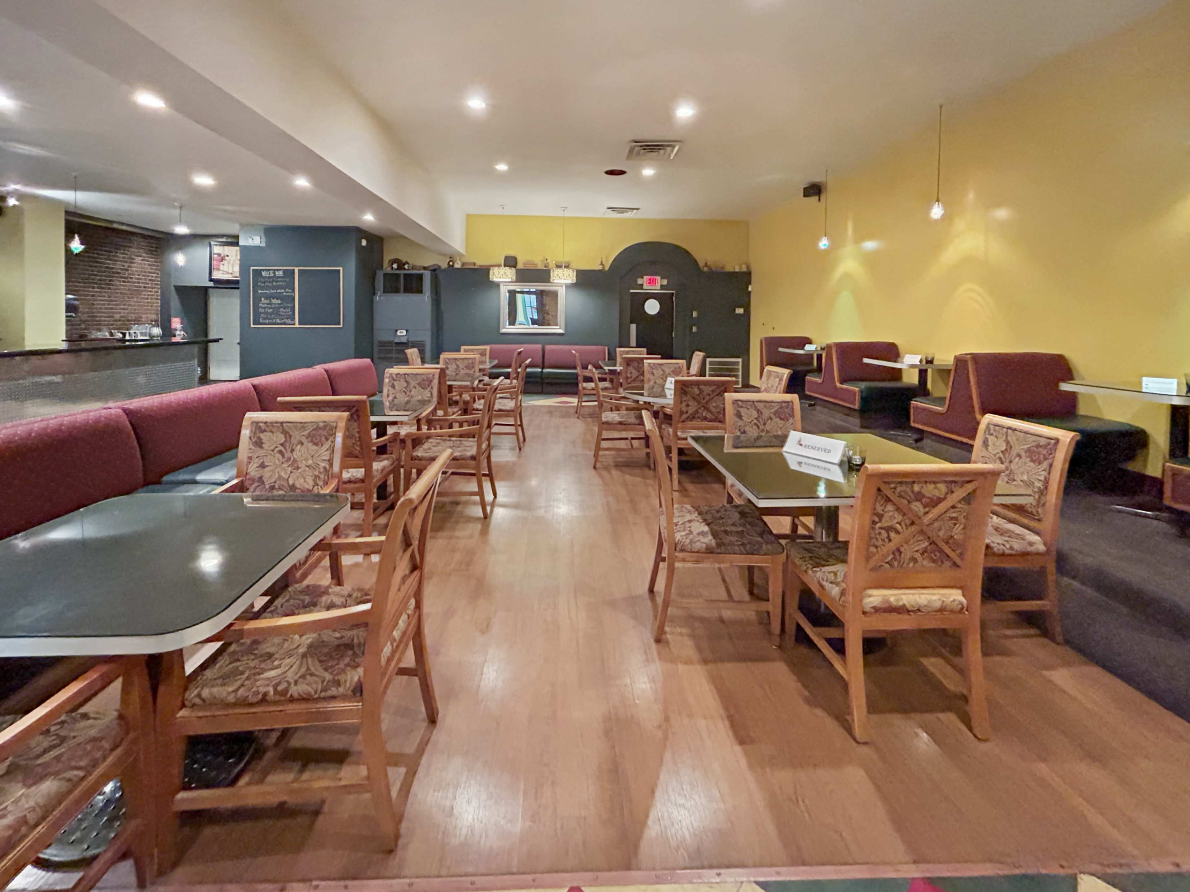 An interior view of a restaurant features wooden tables and chairs arranged neatly in a spacious, brightly lit room with yellow and gray walls.