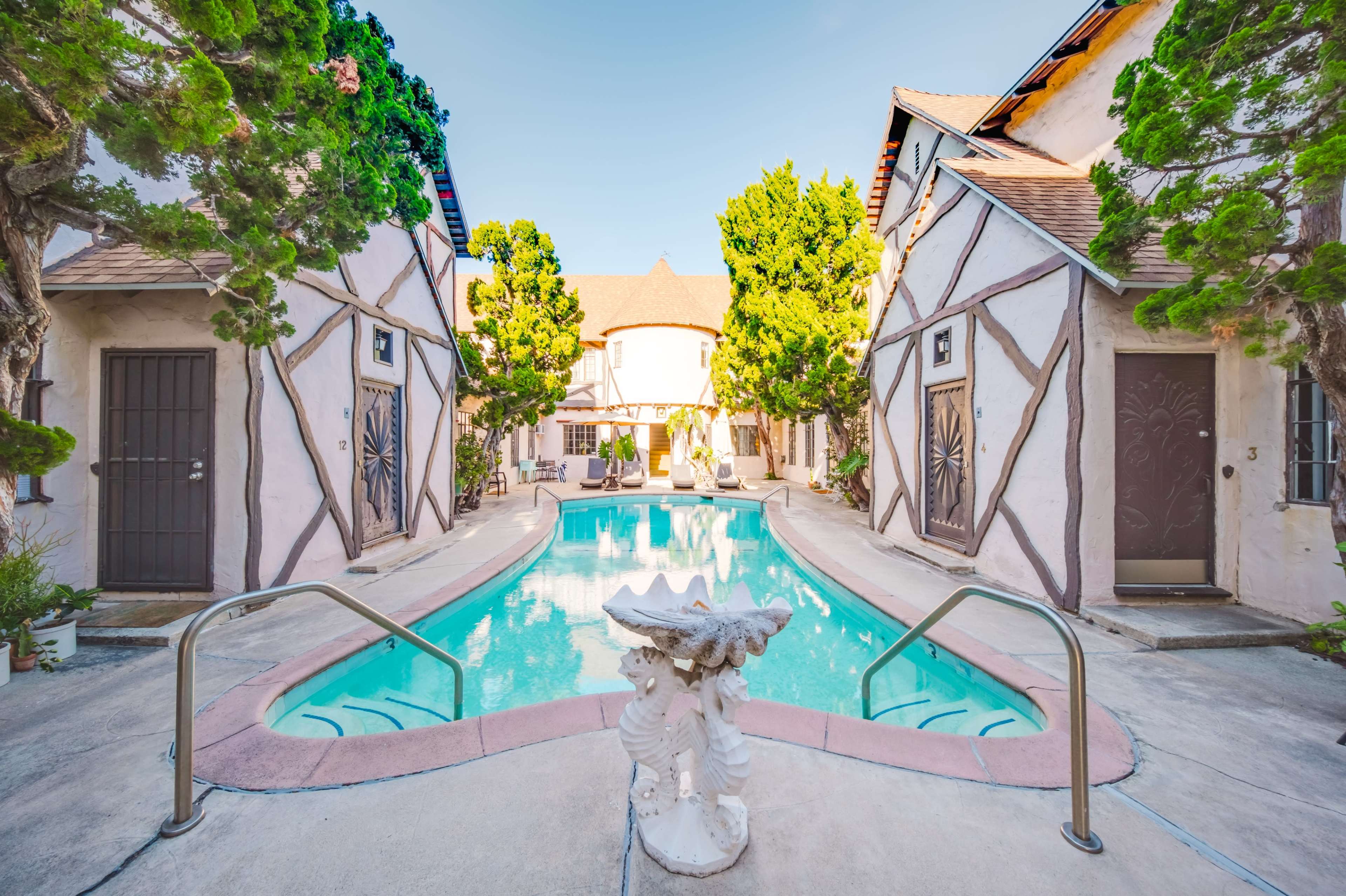 The image shows a courtyard with a swimming pool surrounded by two buildings featuring a Tudor-style architectural design.