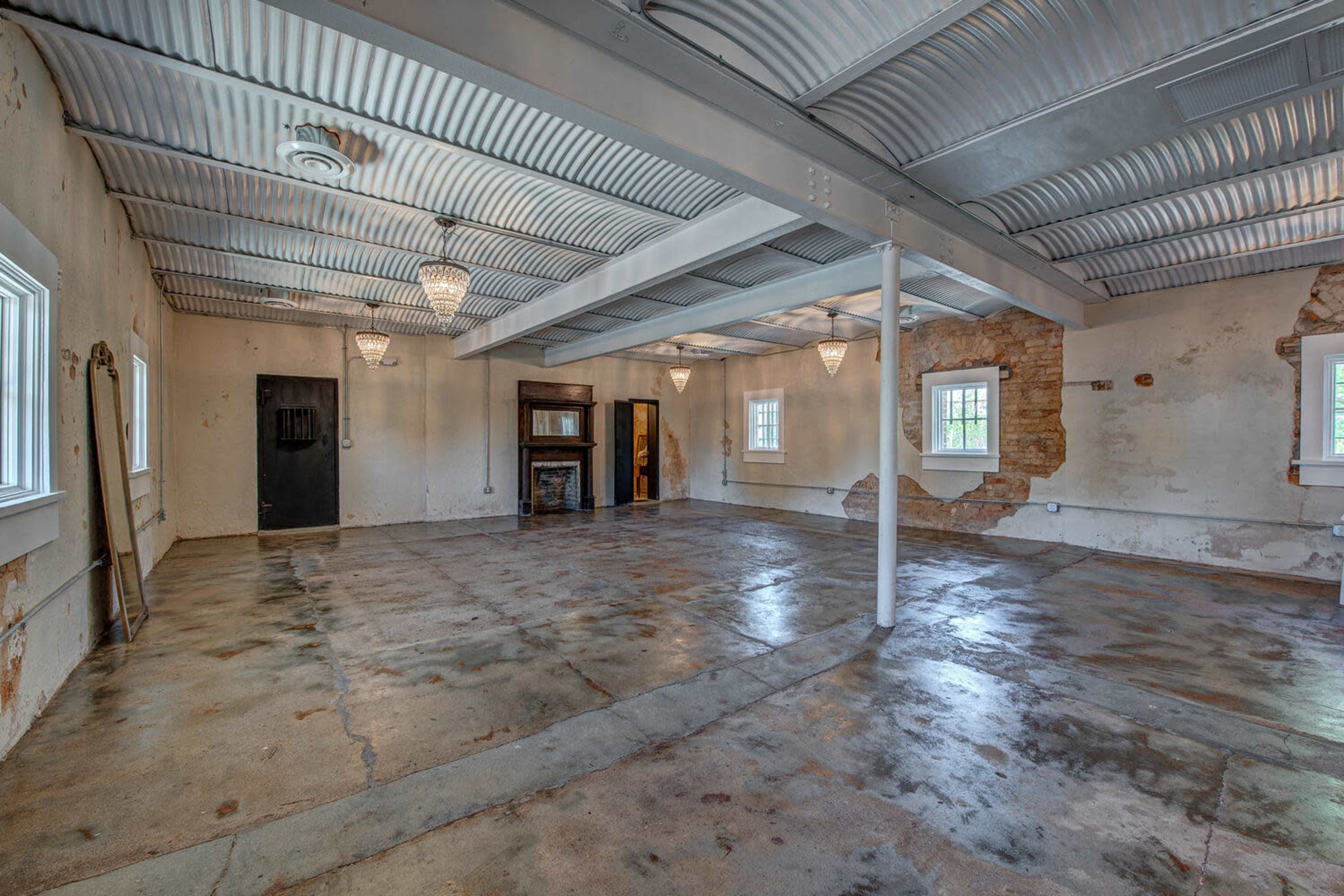 A large, empty room with concrete flooring, exposed walls, and several windows providing natural light.