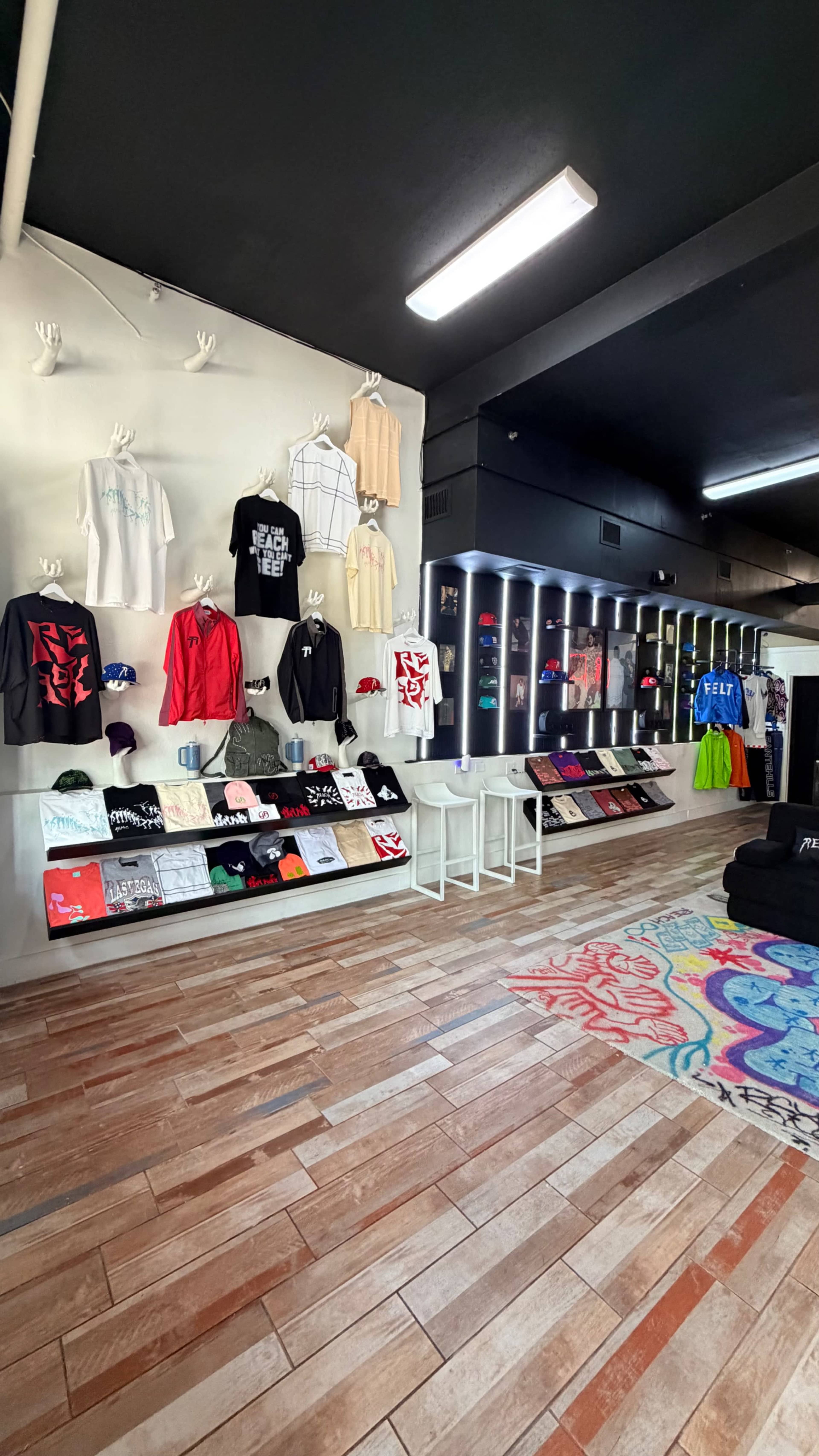 The image shows an interior of a clothing store with a variety of t-shirts, hats, and other apparel displayed on walls and racks.