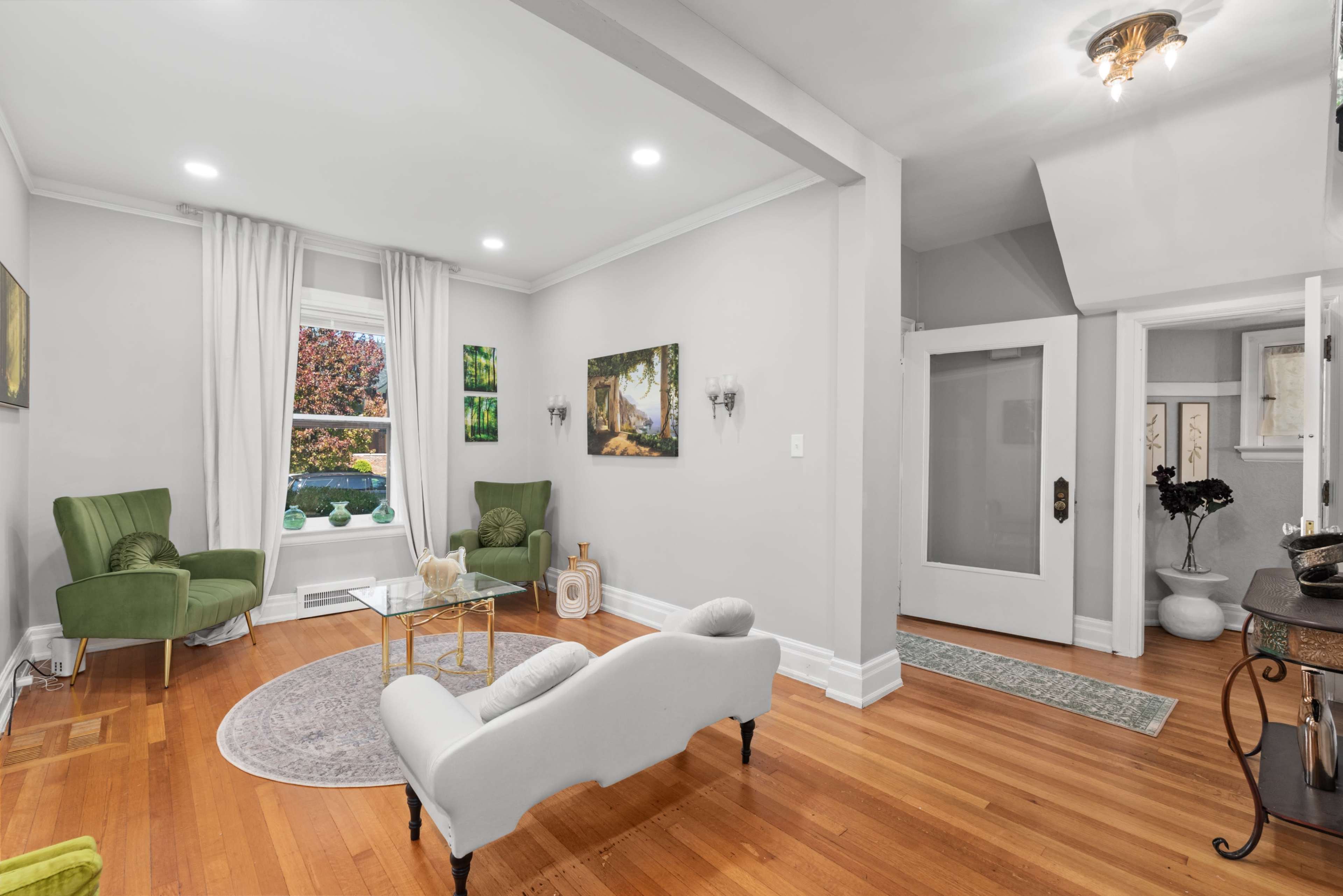 A well-lit living room with two green armchairs, a coffee table, and hardwood flooring, featuring a frosted glass door leading to another room.
