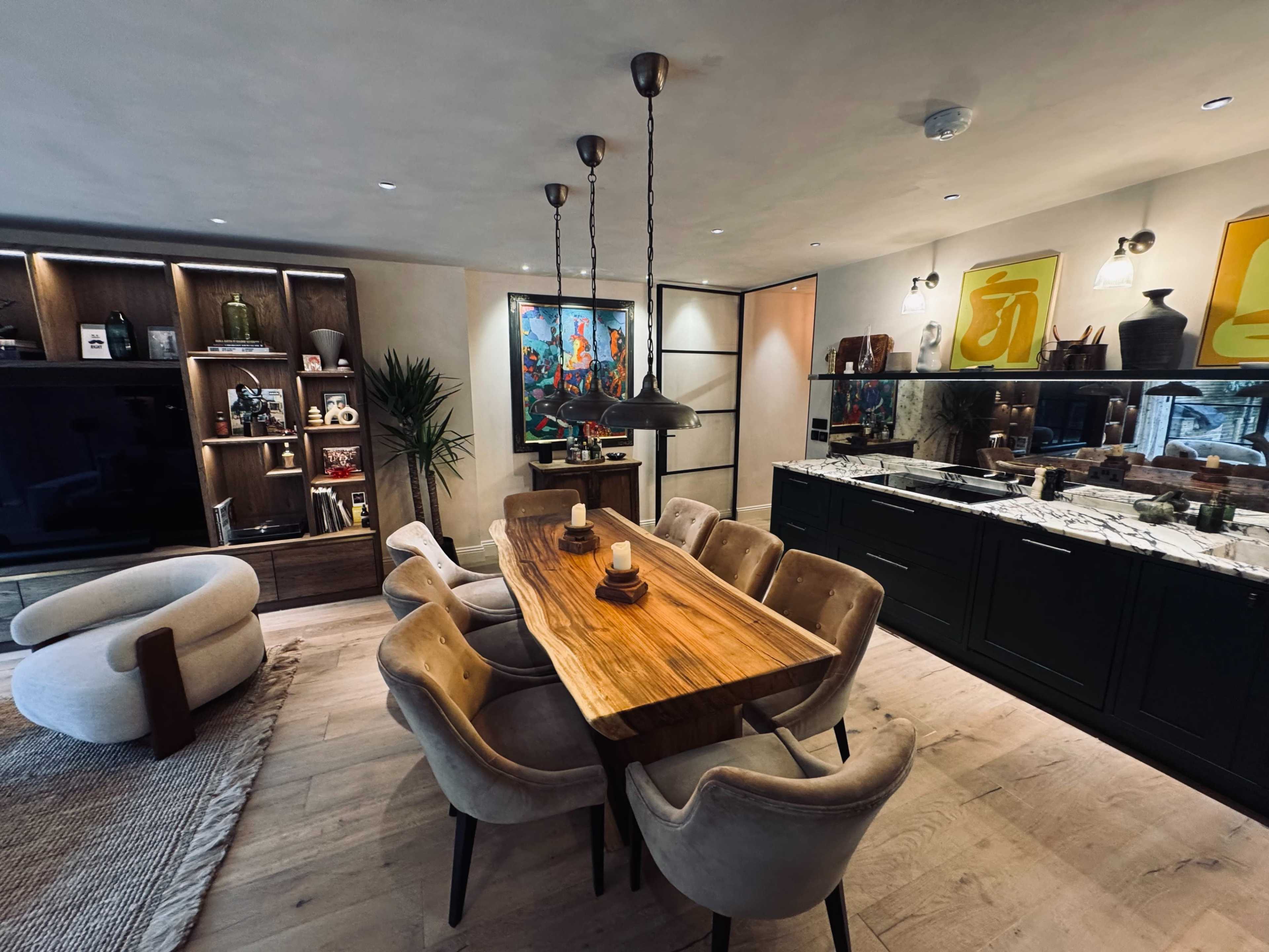 A modern dining area features a wooden table surrounded by upholstered chairs, with a display cabinet and artwork on the walls.