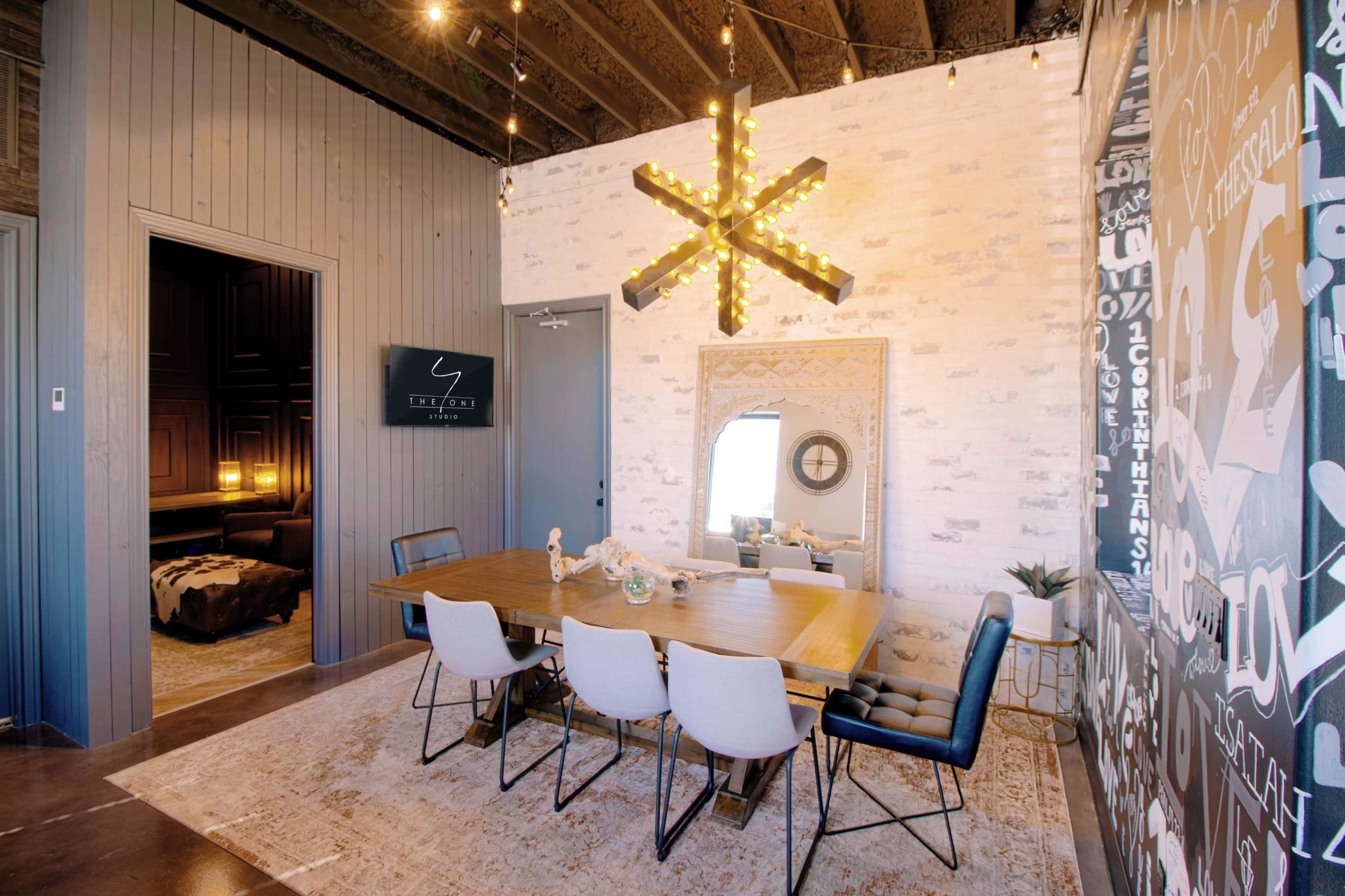 A dining area features a wooden table with white and black chairs, illuminated by a star-shaped light fixture against a textured wall.