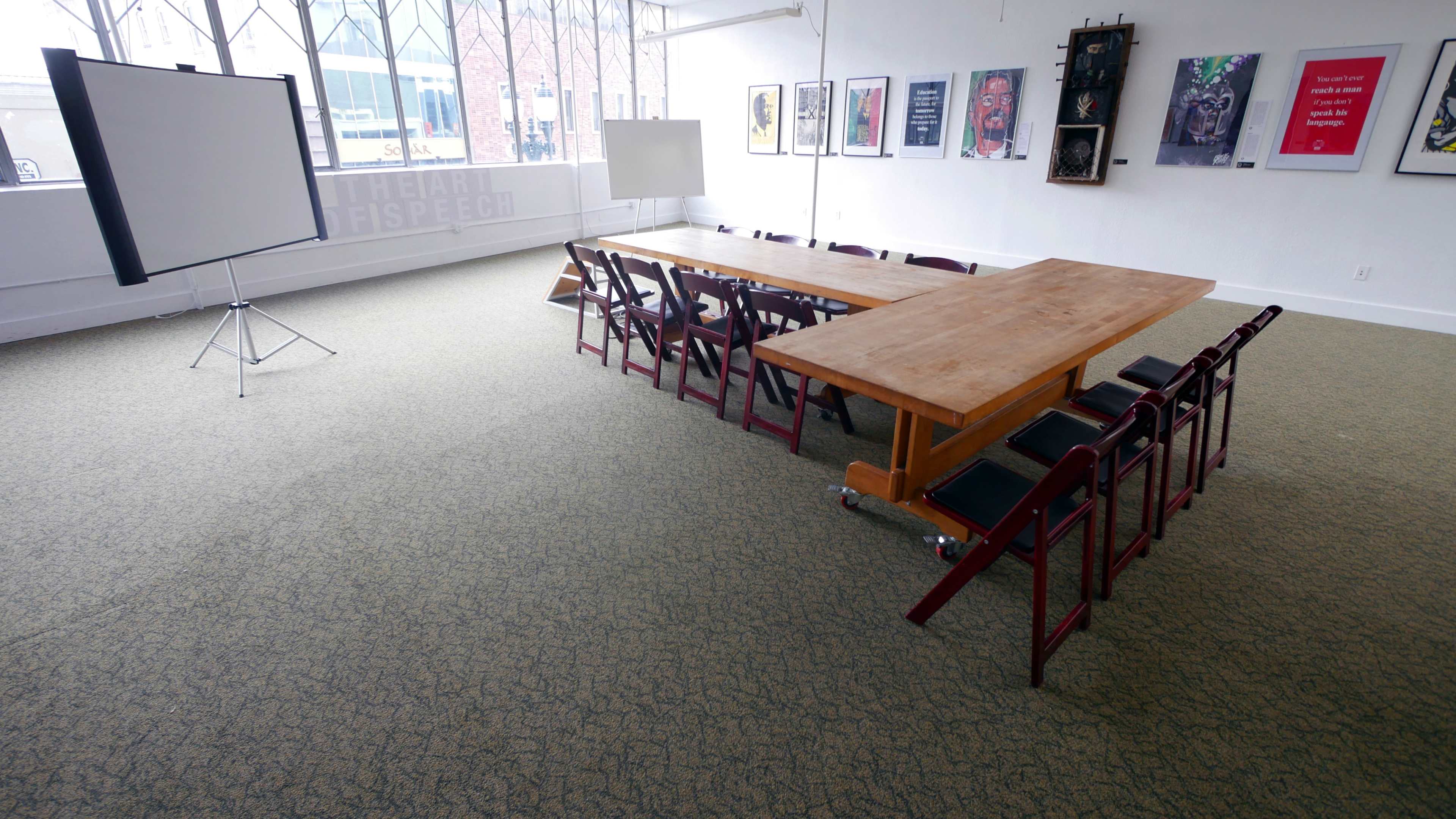 A spacious meeting room with a large wooden table, surrounded by folding chairs, and artwork on the walls.
