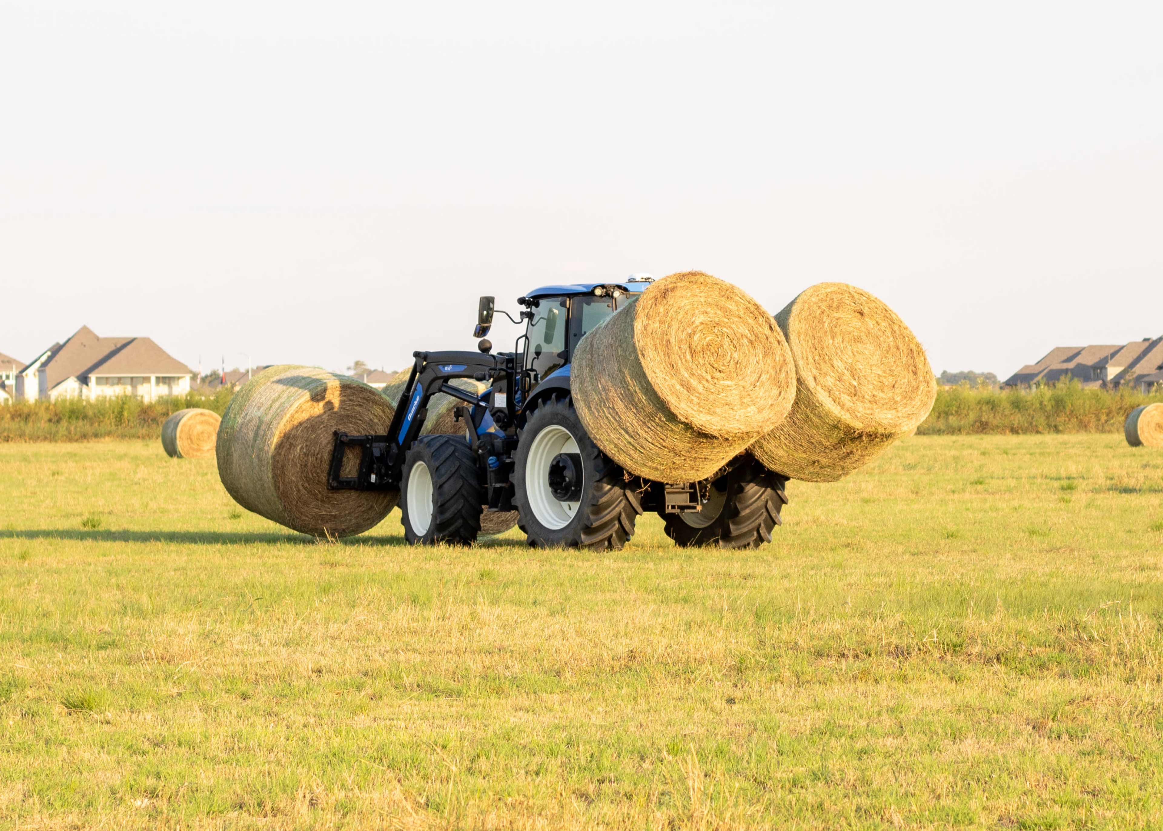 A tractor is transporting two large hay bales across a grassy field.