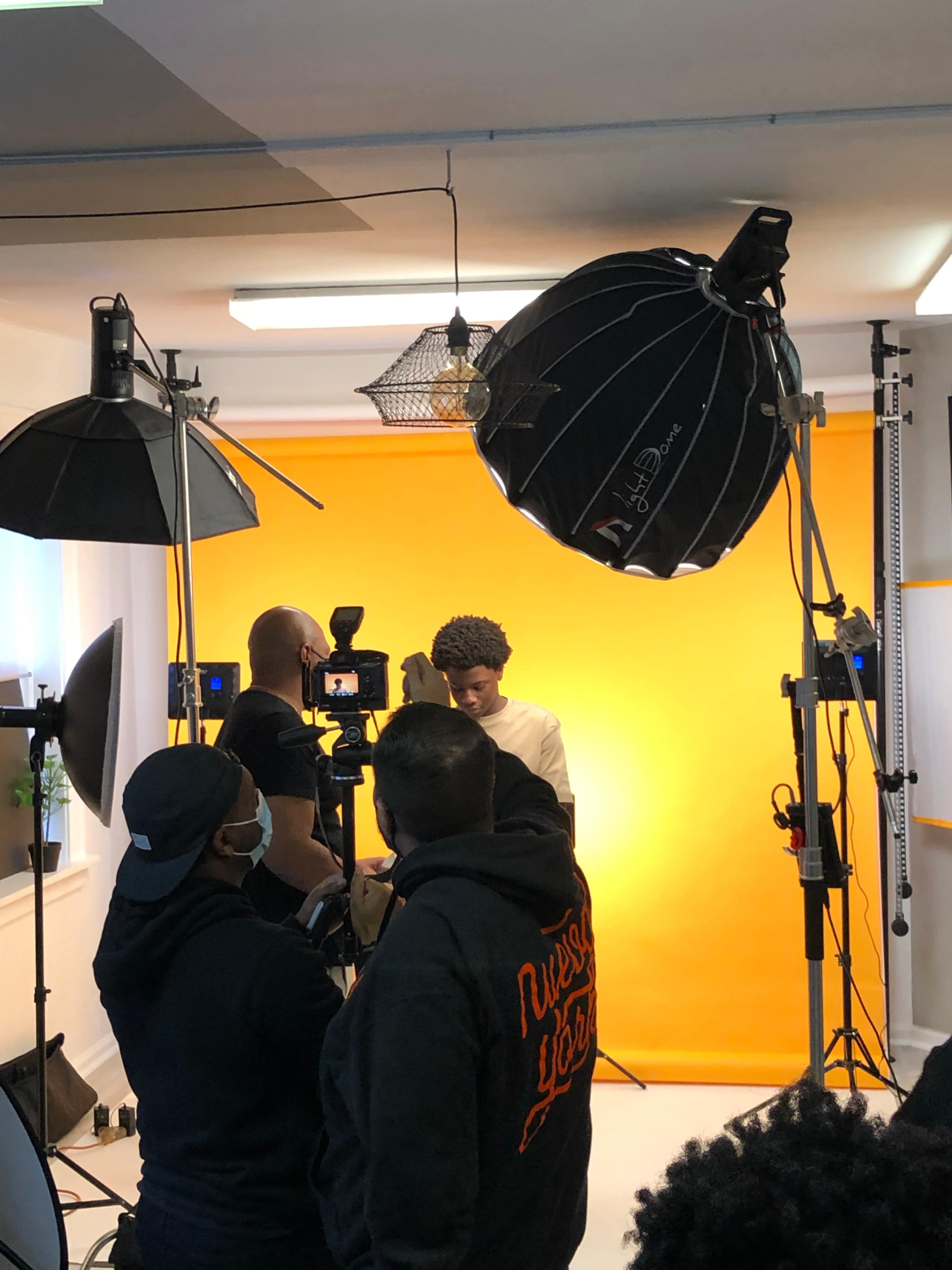 A photographer captures a subject posing in front of a bright orange backdrop in a studio setting.