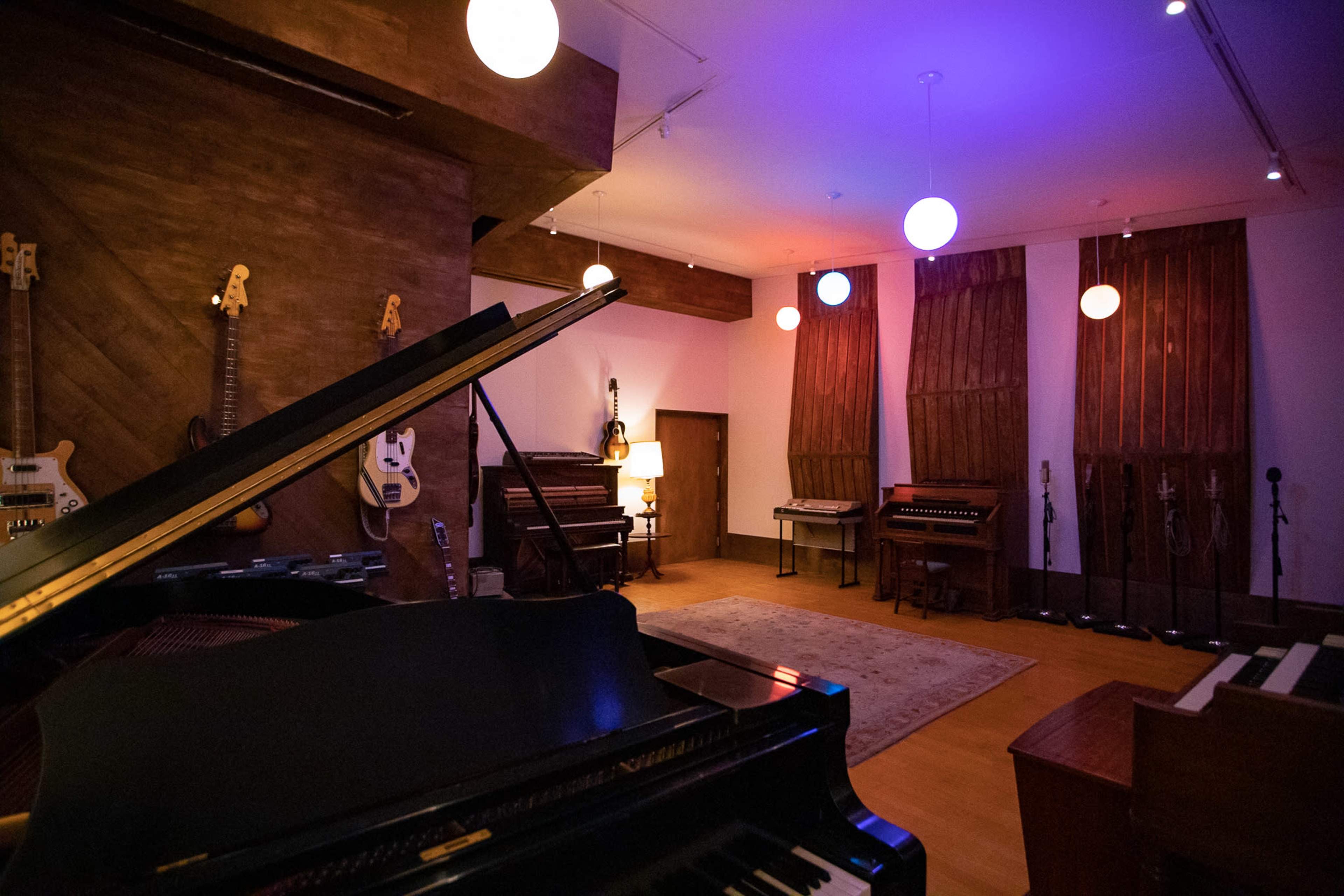 A spacious music studio featuring a grand piano, various instruments on display, and soft lighting from hanging orbs.