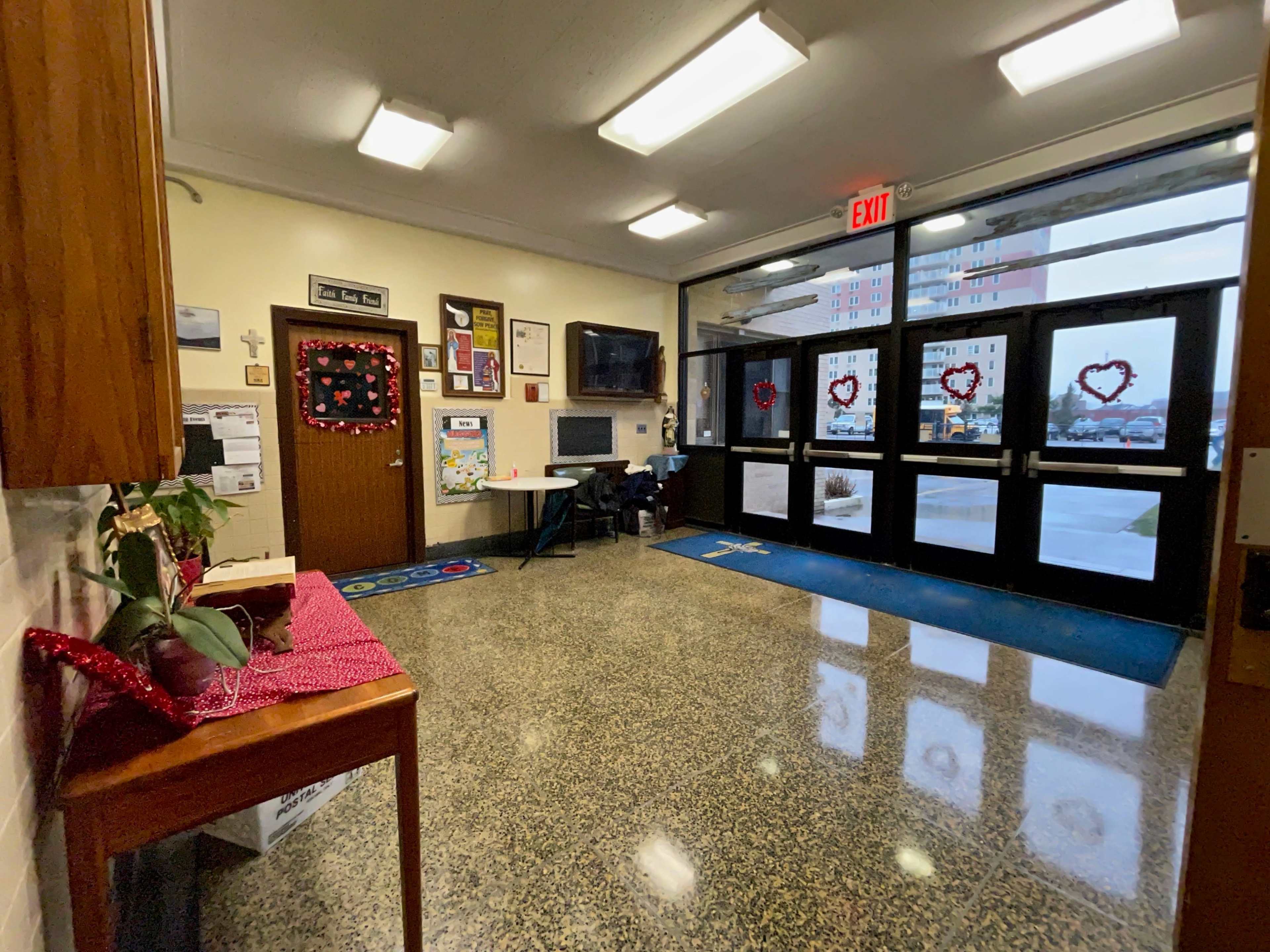 The entrance area features a tiled floor, a wooden table with a plant, and decorated windows with heart shapes, leading to a glass door.