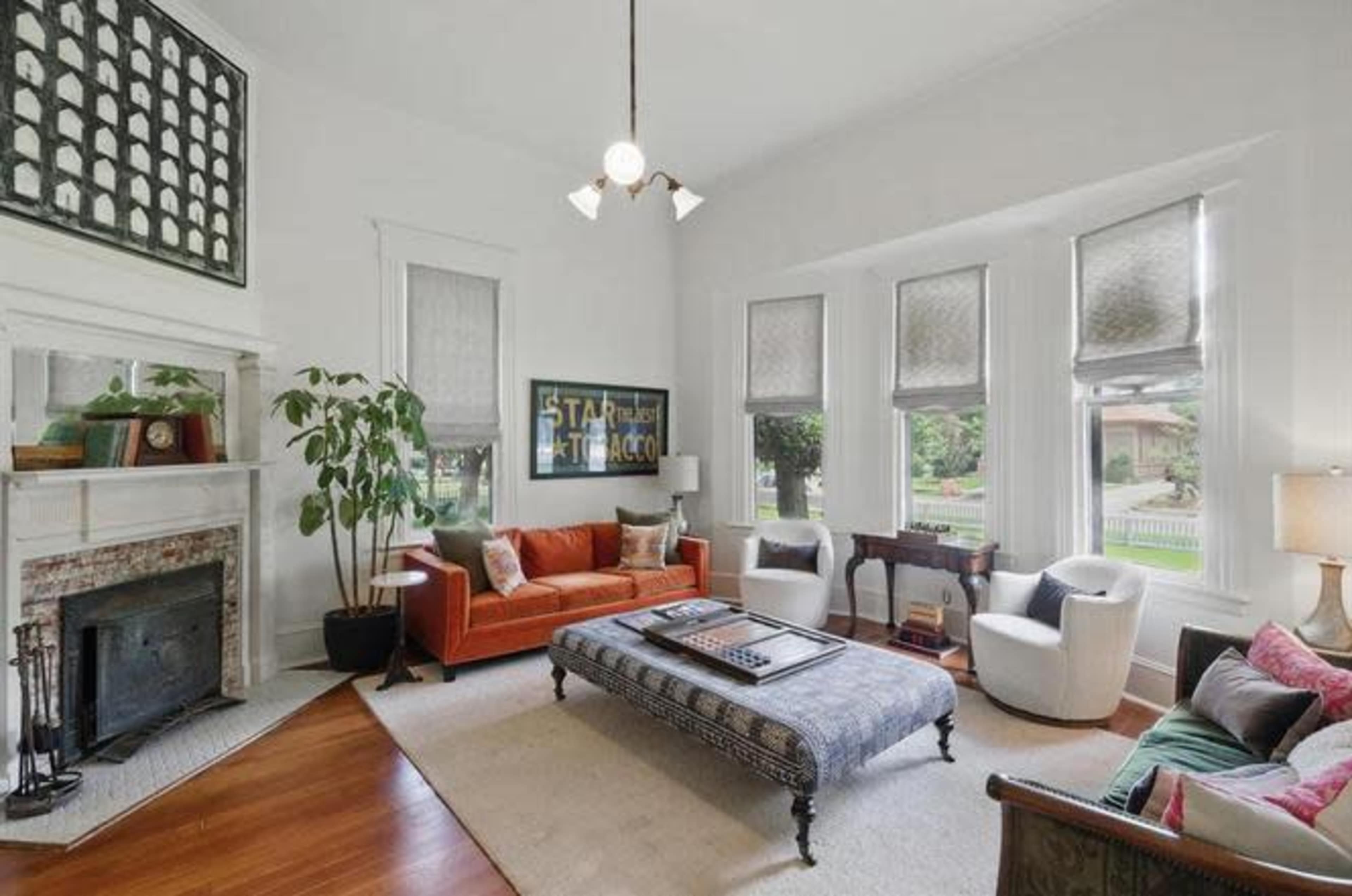 The living room features a mix of modern and vintage furniture, with a large orange sofa, a patterned coffee table, and multiple windows allowing natural light to enter.