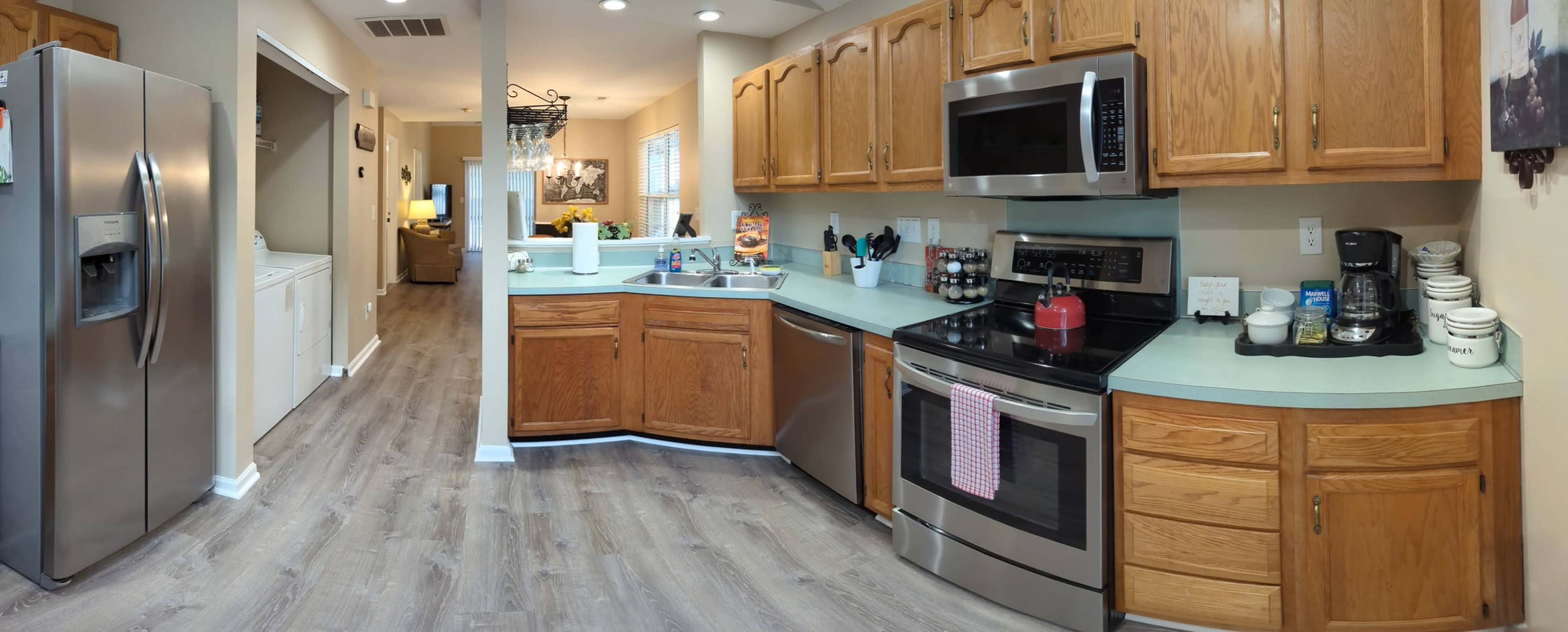 A kitchen with wooden cabinetry, stainless steel appliances, and a light-colored countertop along with a view into an adjacent living area.