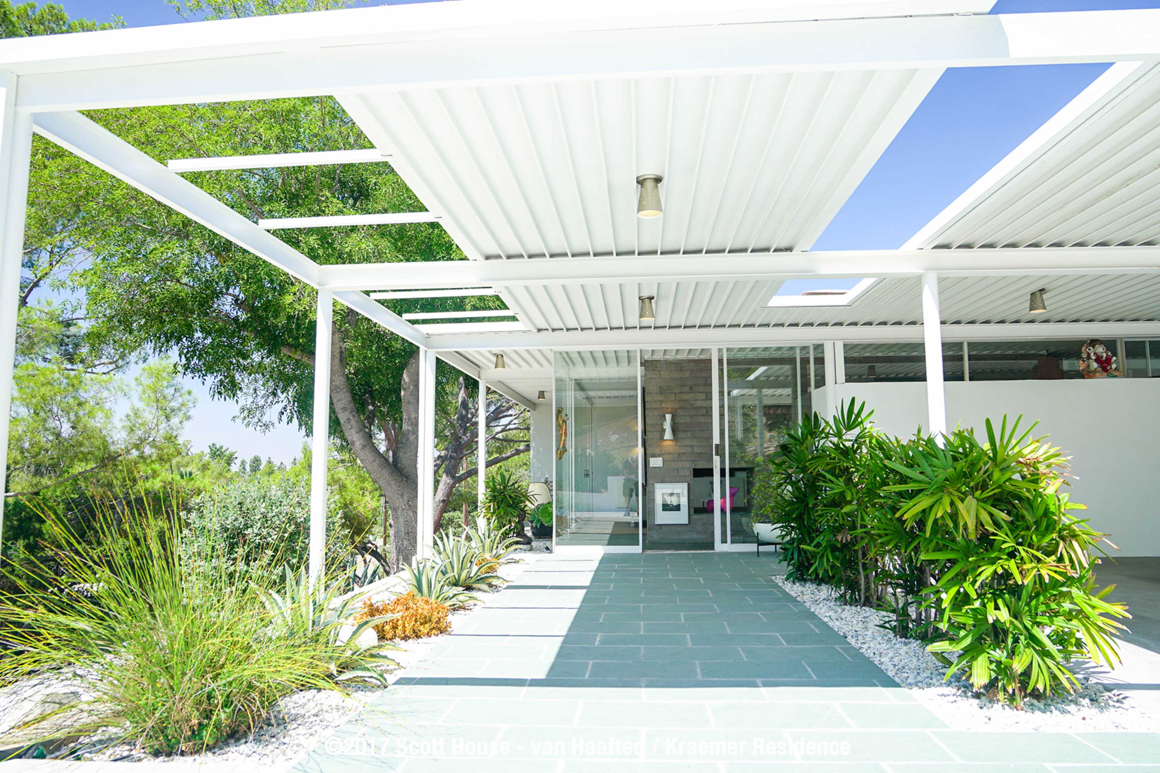 A modern house with a covered patio, surrounded by landscaped greenery and stone pathways.
