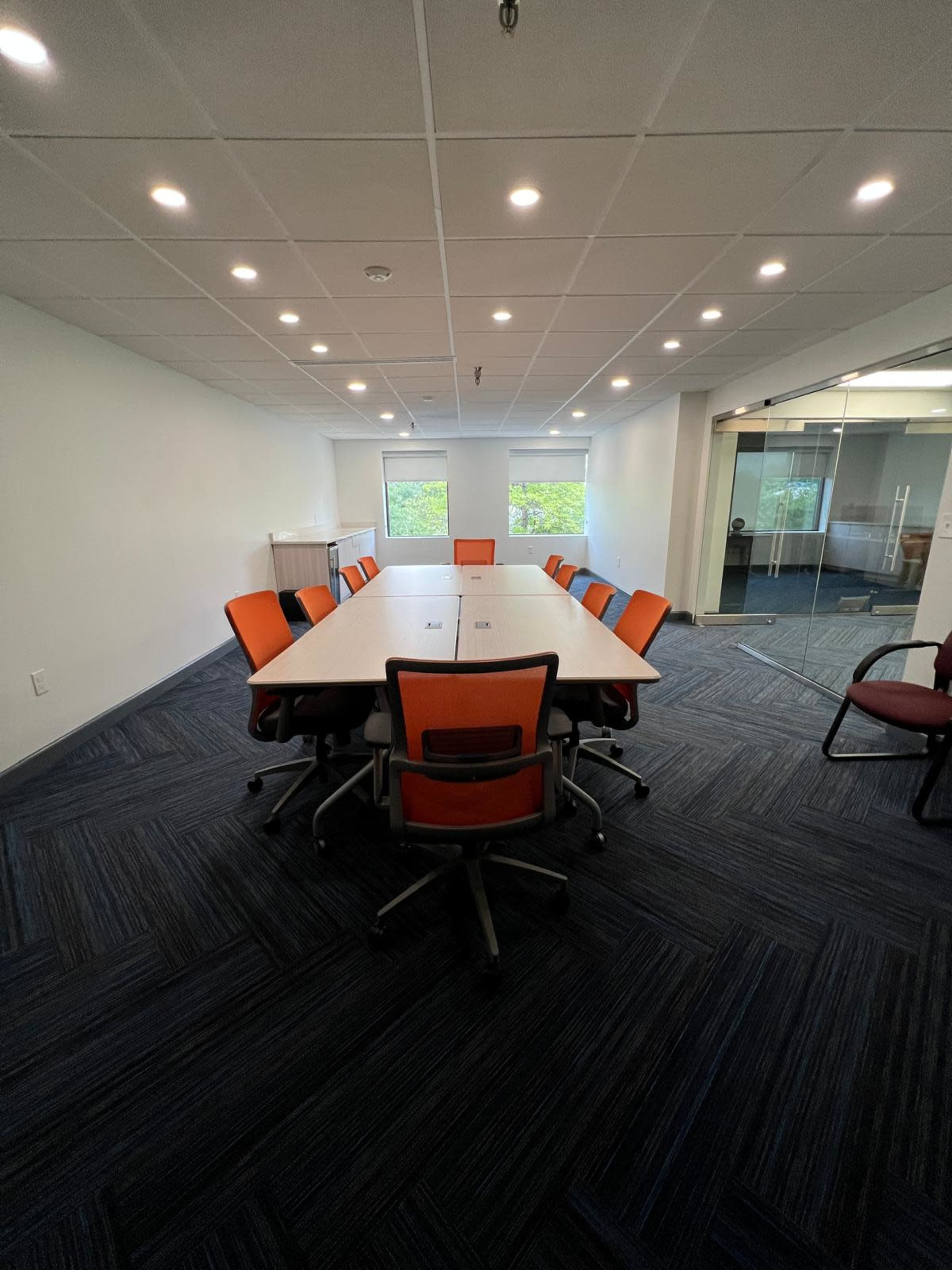 A spacious conference room features a large, rectangular table surrounded by orange and gray chairs under bright overhead lighting.