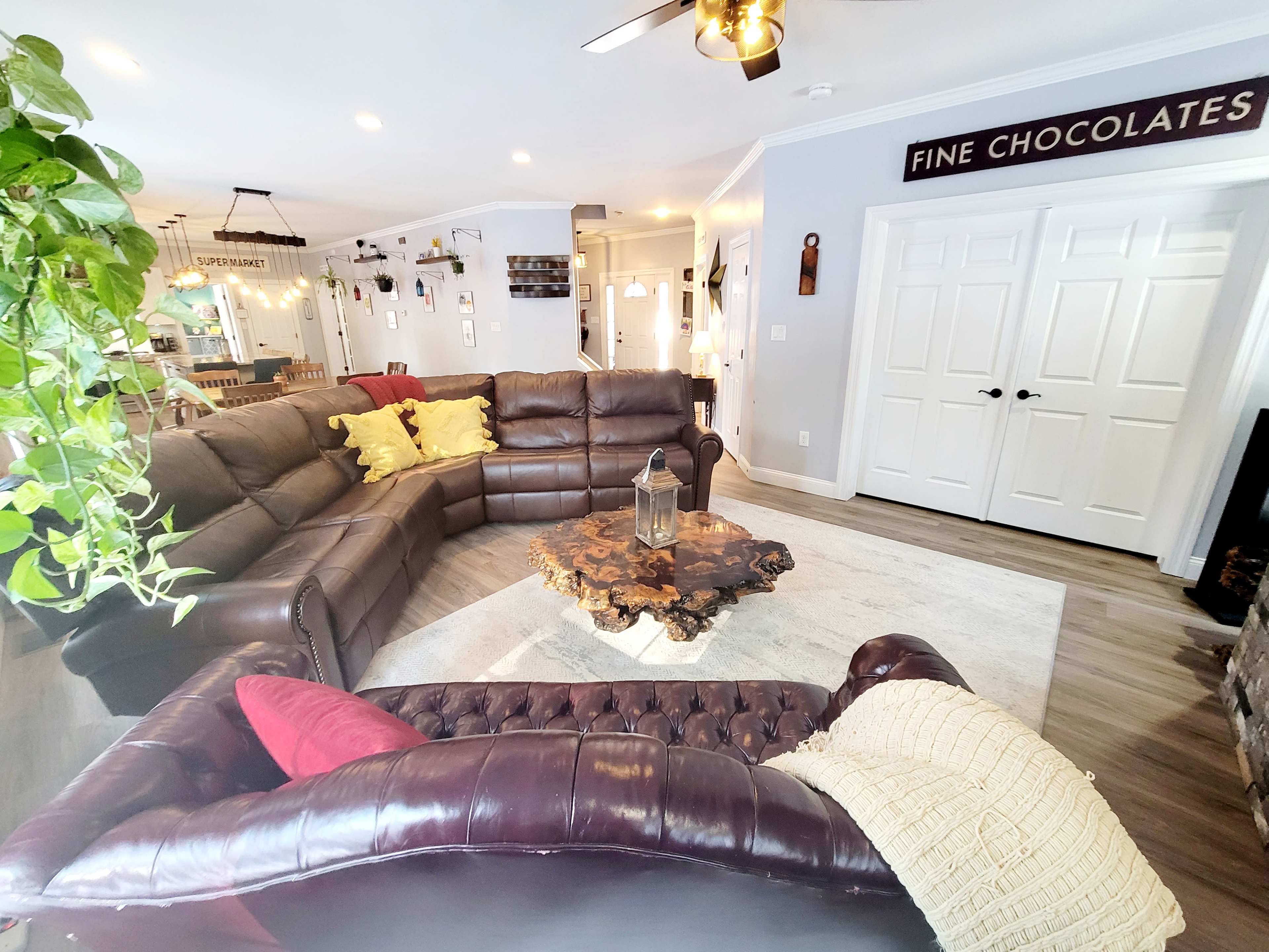 A spacious living room features a large brown leather sectional sofa, a wooden coffee table, and decorative plants.