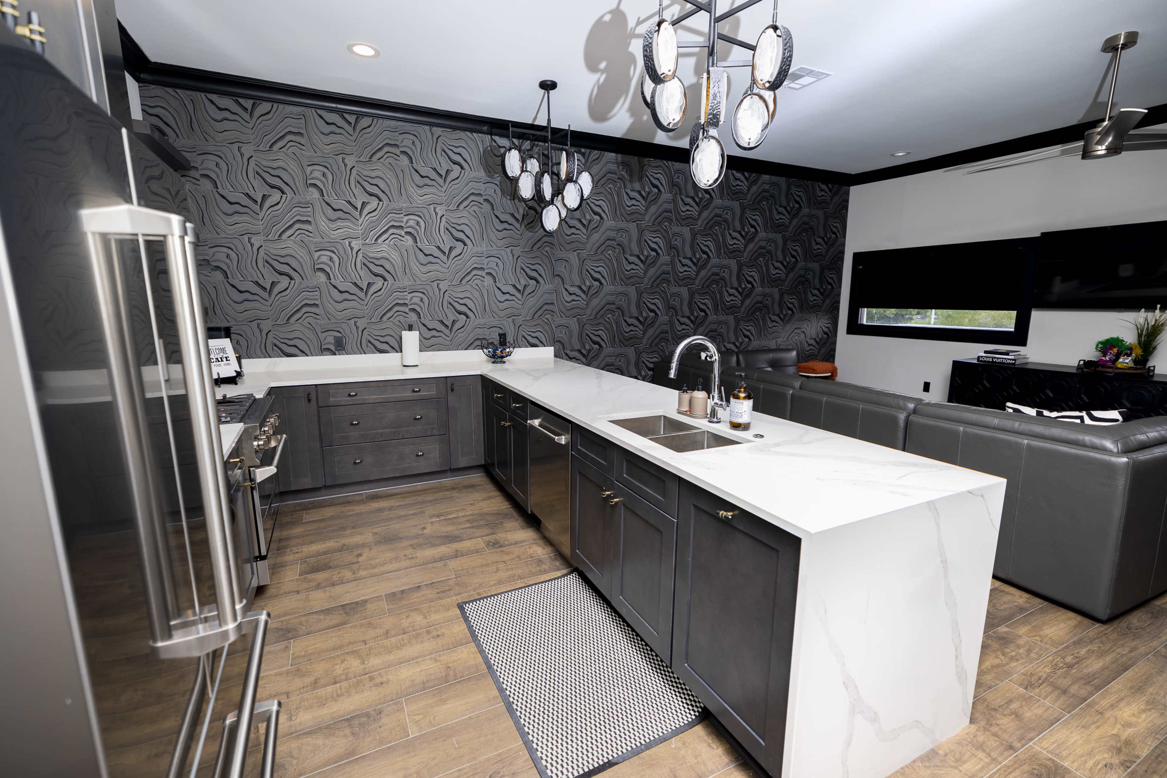 The image shows a modern kitchen with a central island, dark cabinetry, and a patterned accent wall.