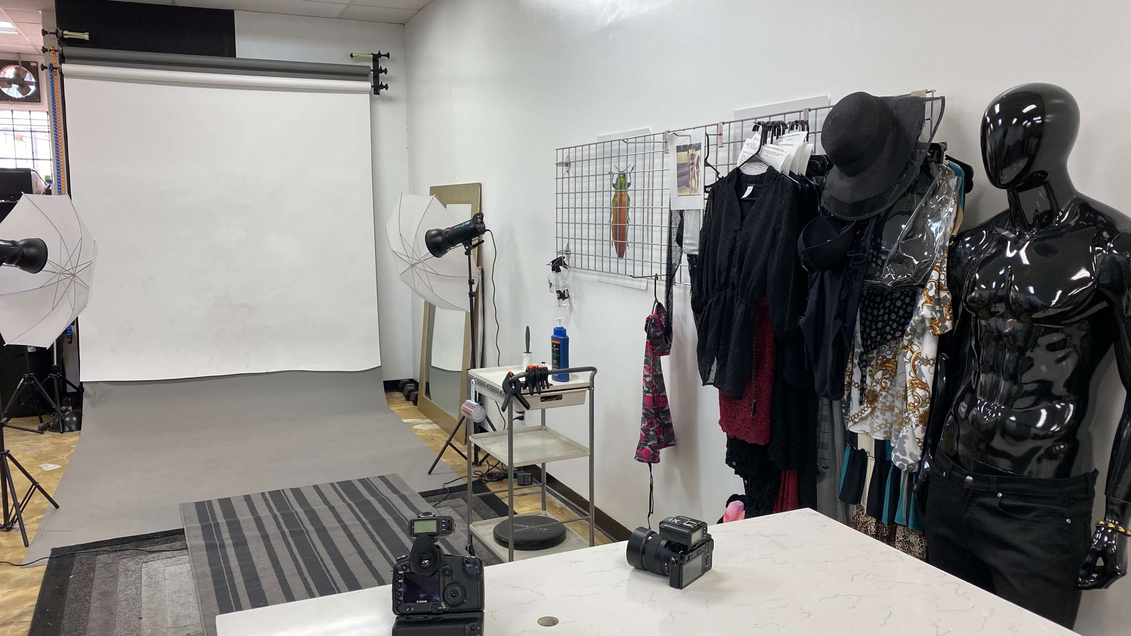 A photography studio features a backdrop, lighting equipment, and clothing displays alongside cameras on a table.