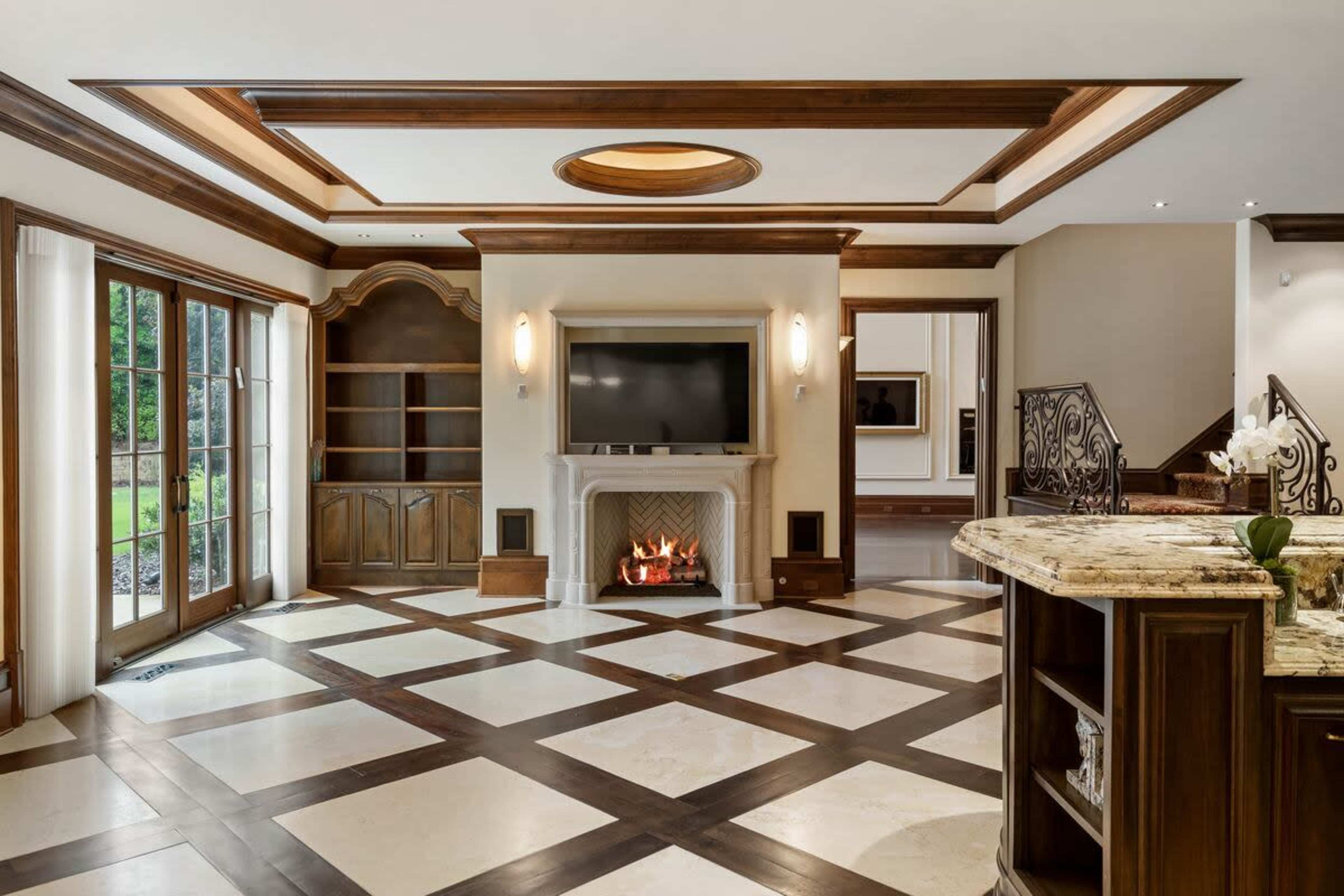 The image shows a spacious living room with a fireplace, a large television mounted above the mantel, and distinct patterned flooring.