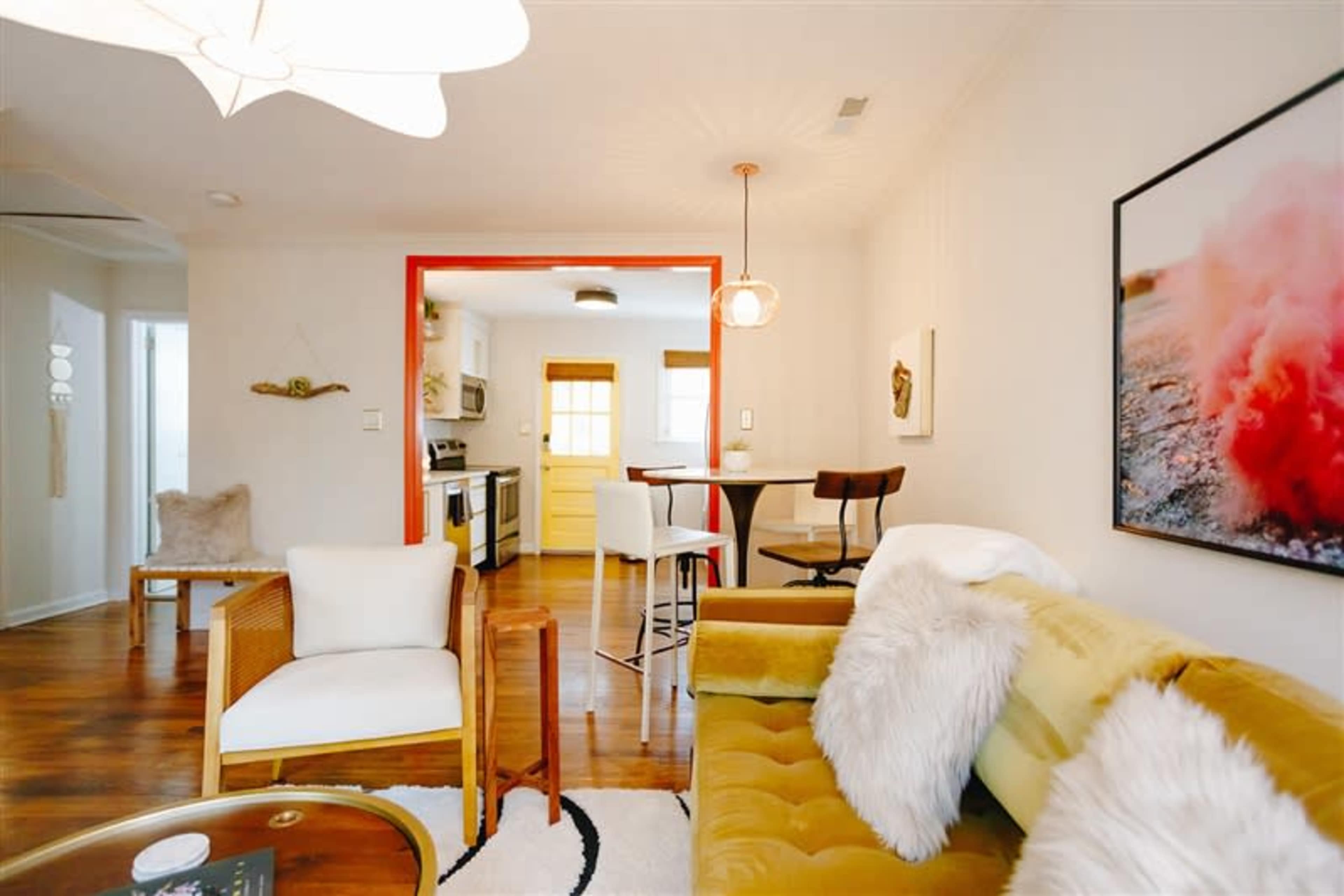 A cozy living area with a green couch, a small dining table in the background, and a kitchen visible through an open doorway.