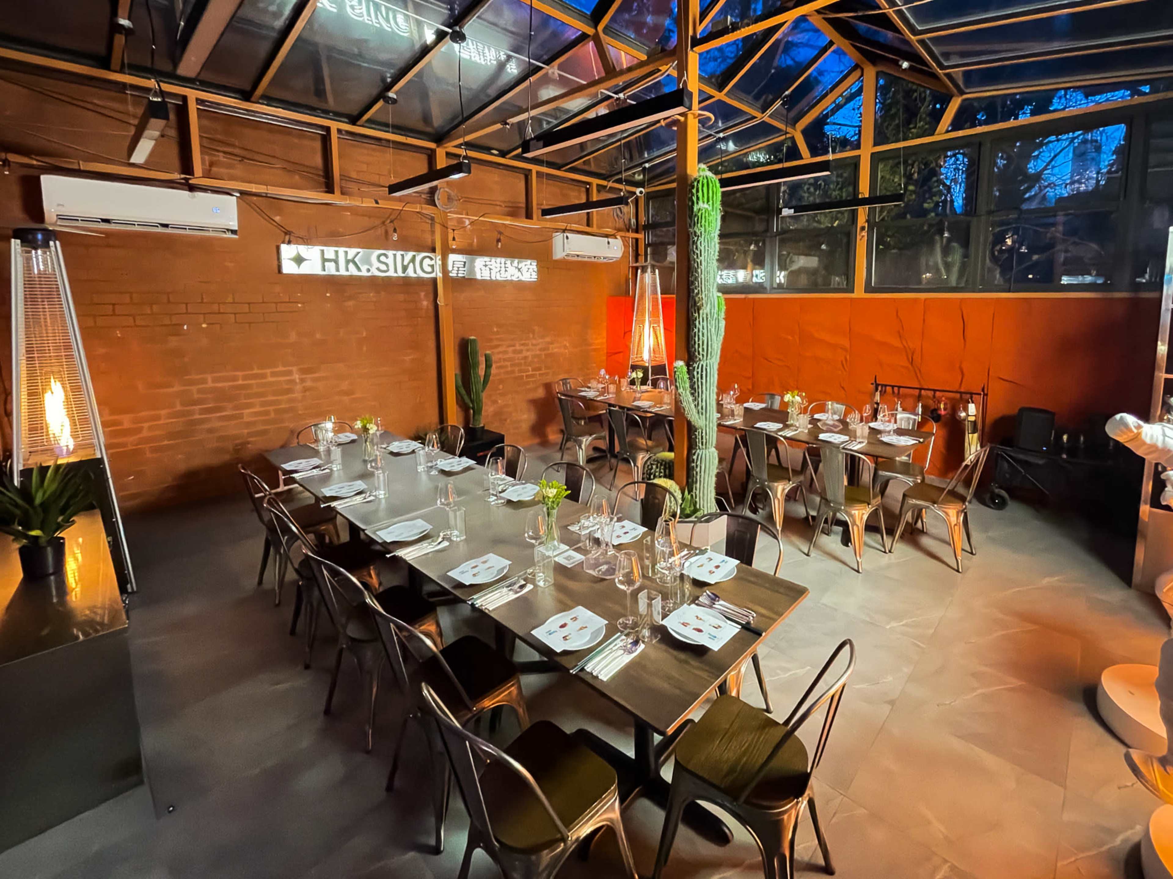 A well-arranged dining area features tables set with cutlery and glassware under a glass ceiling, illuminated by ambient lighting and decorative plants.