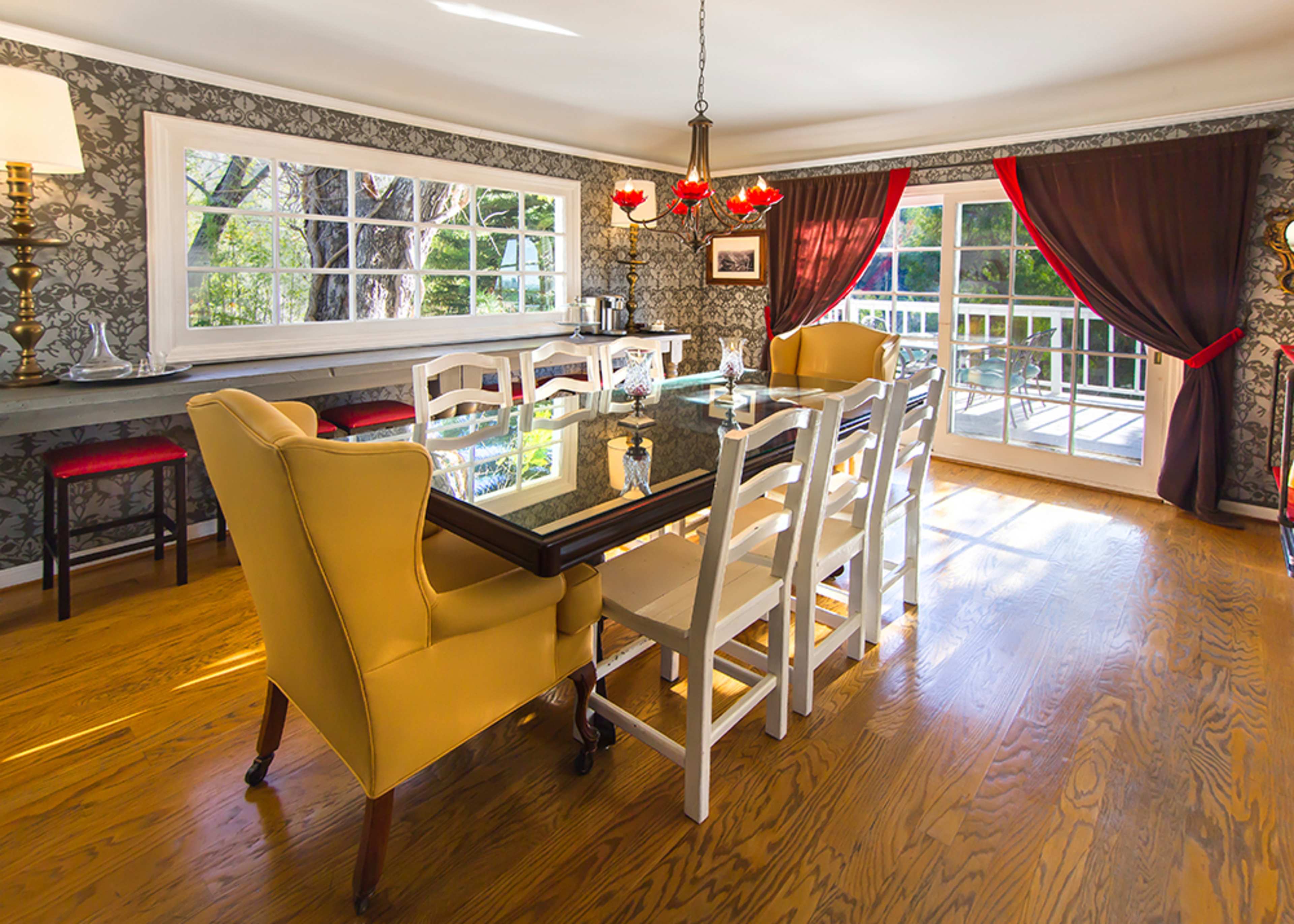 A spacious dining room features a large table surrounded by white and yellow chairs, with large windows allowing natural light to enter.