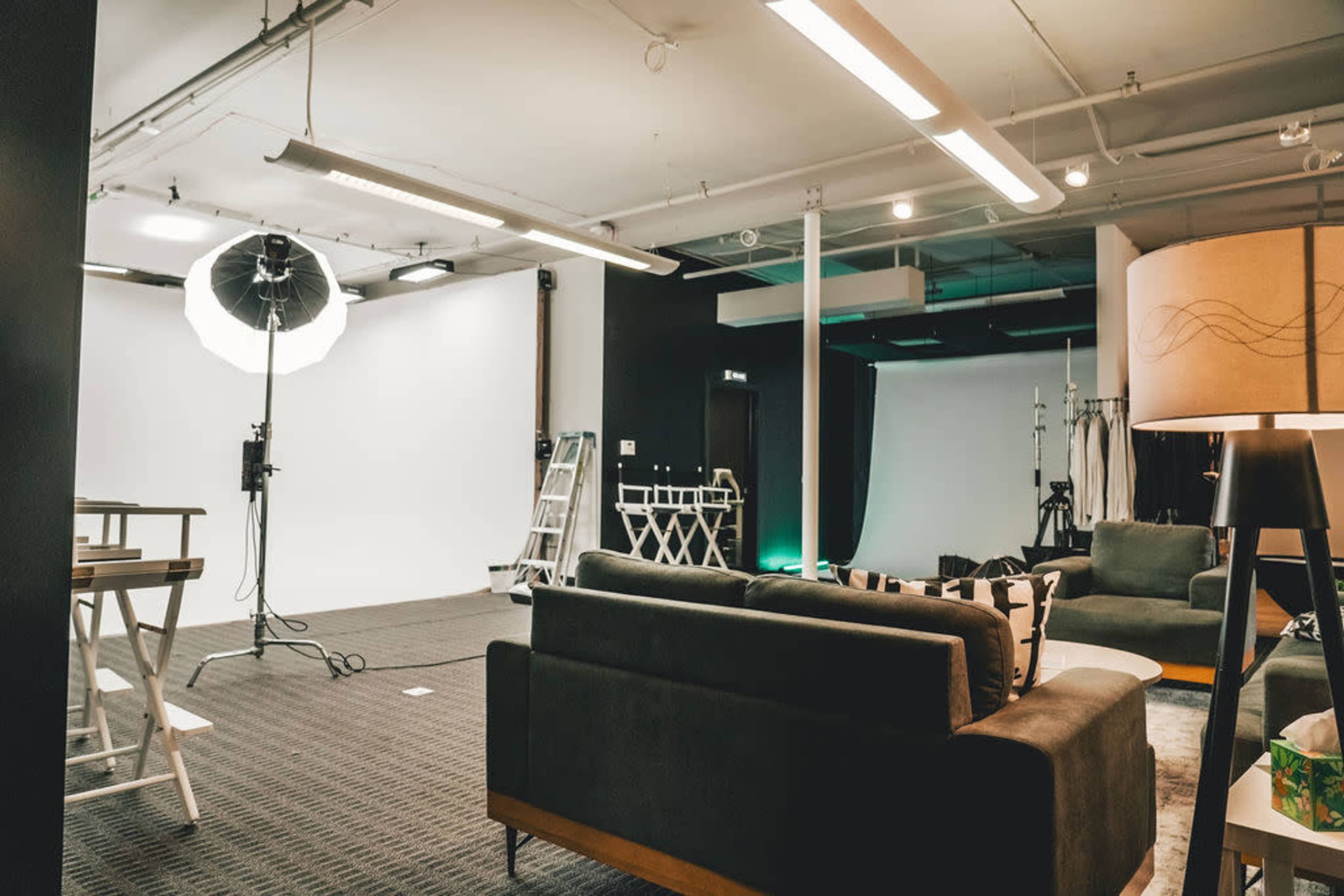 A photography studio with a white backdrop, lighting equipment, and seating areas arranged around the space.