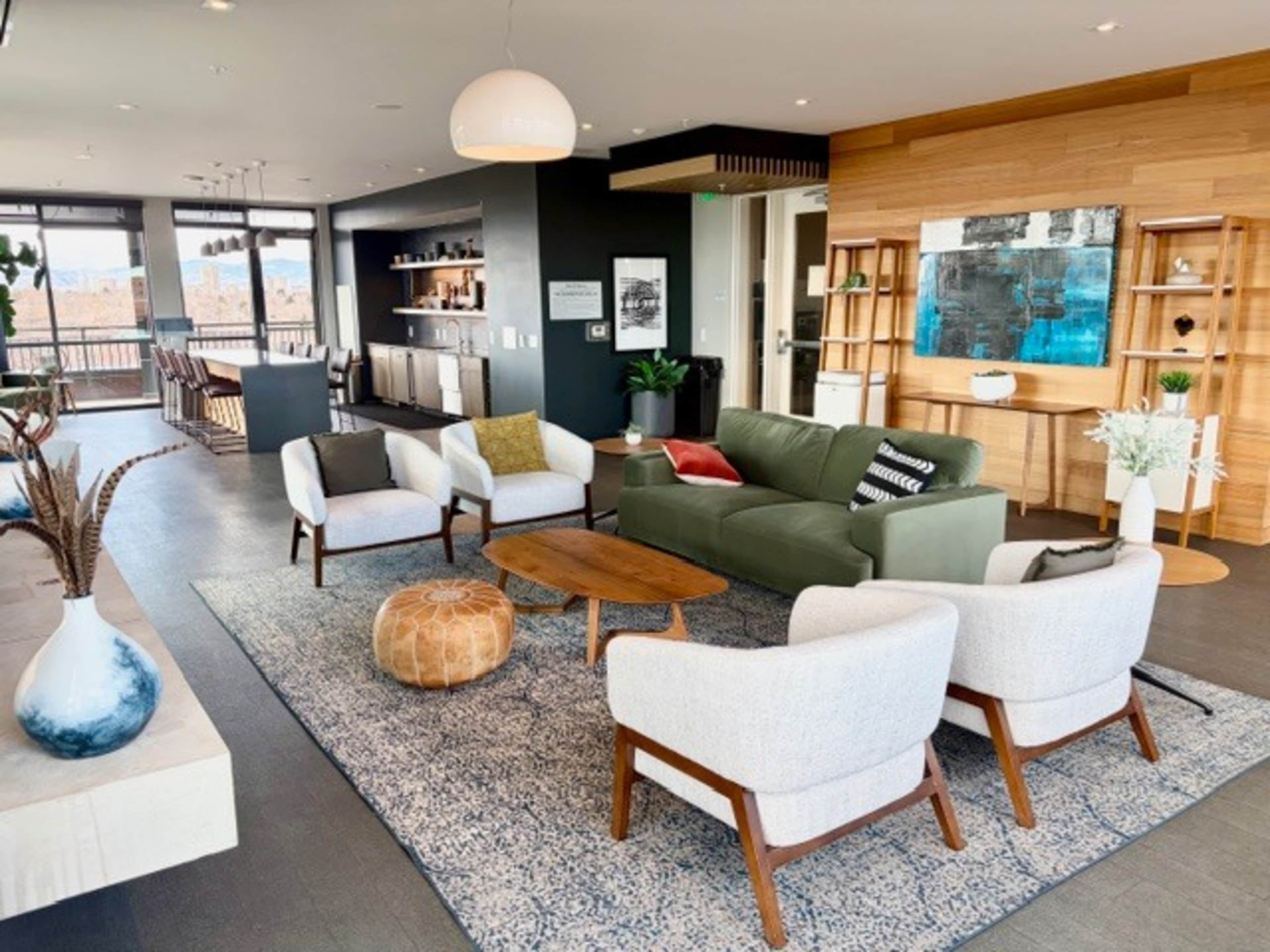 The image depicts a modern living room with a green sofa, four white armchairs, a wooden coffee table, and large windows revealing a scenic view.