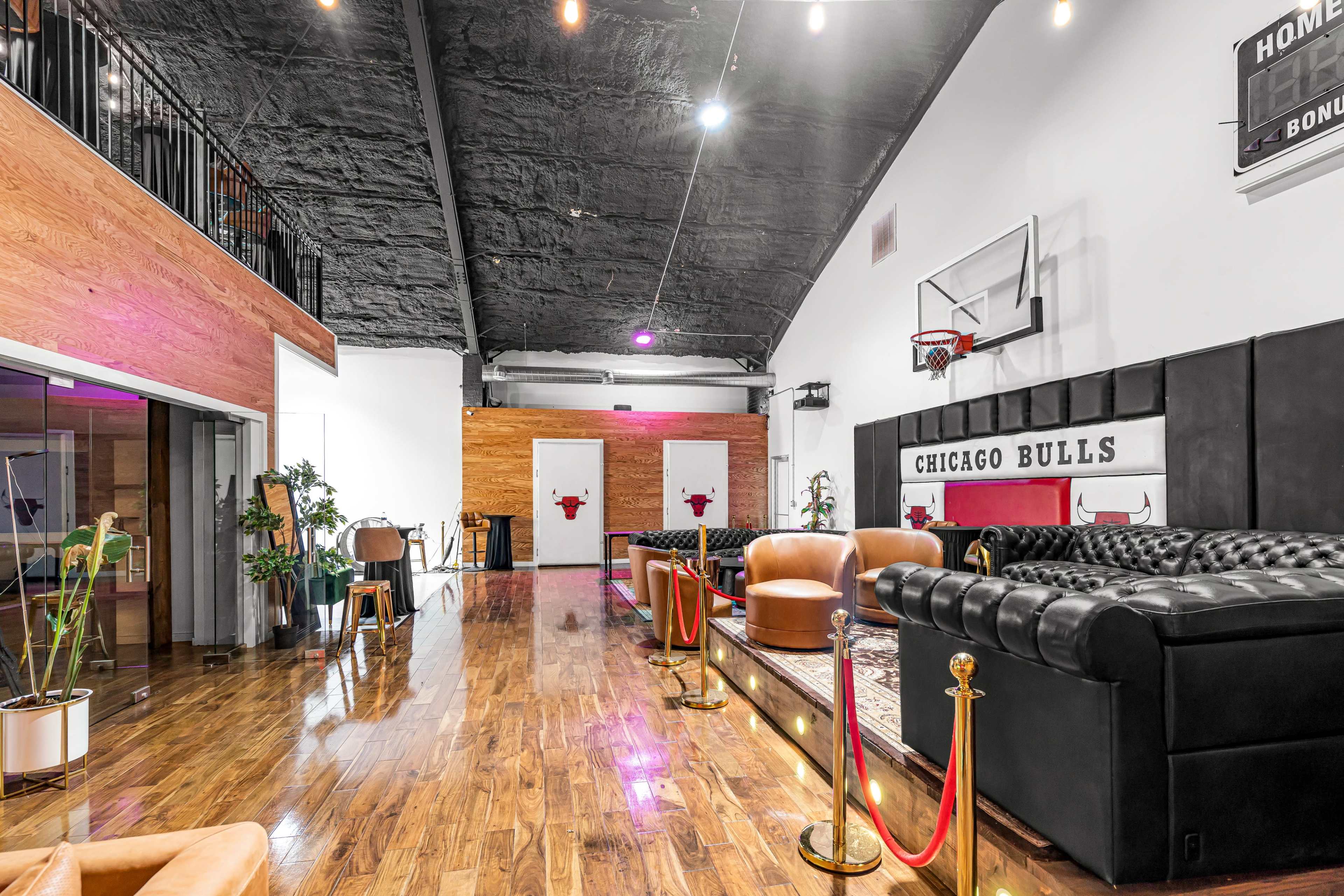 The interior features a modern lounge area with leather seating, polished wooden floors, and a basketball hoop against a wall adorned with Chicago Bulls branding.