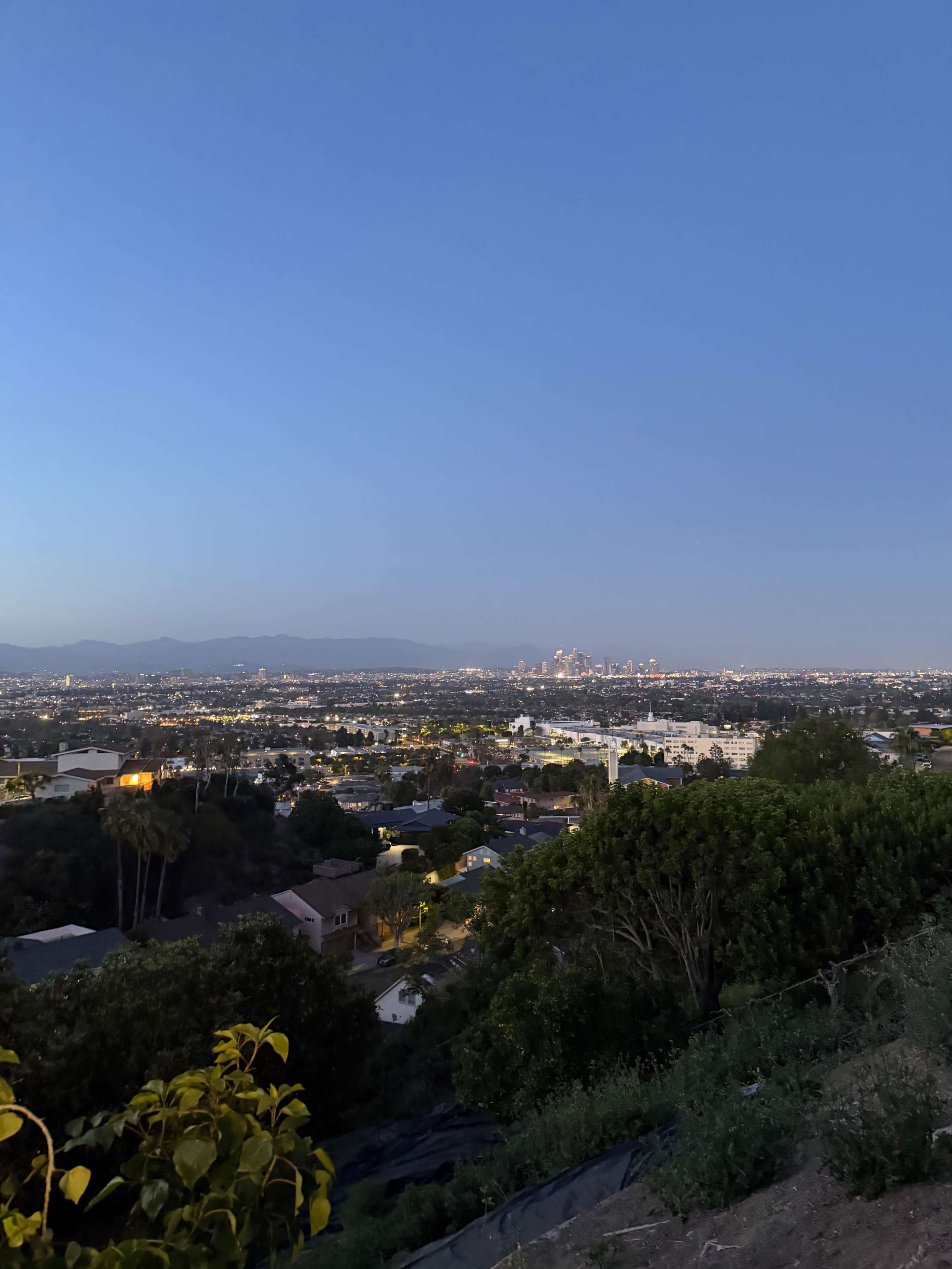 The image shows a panoramic view of a cityscape at dusk, with distant skyscrapers illuminated against the twilight sky.