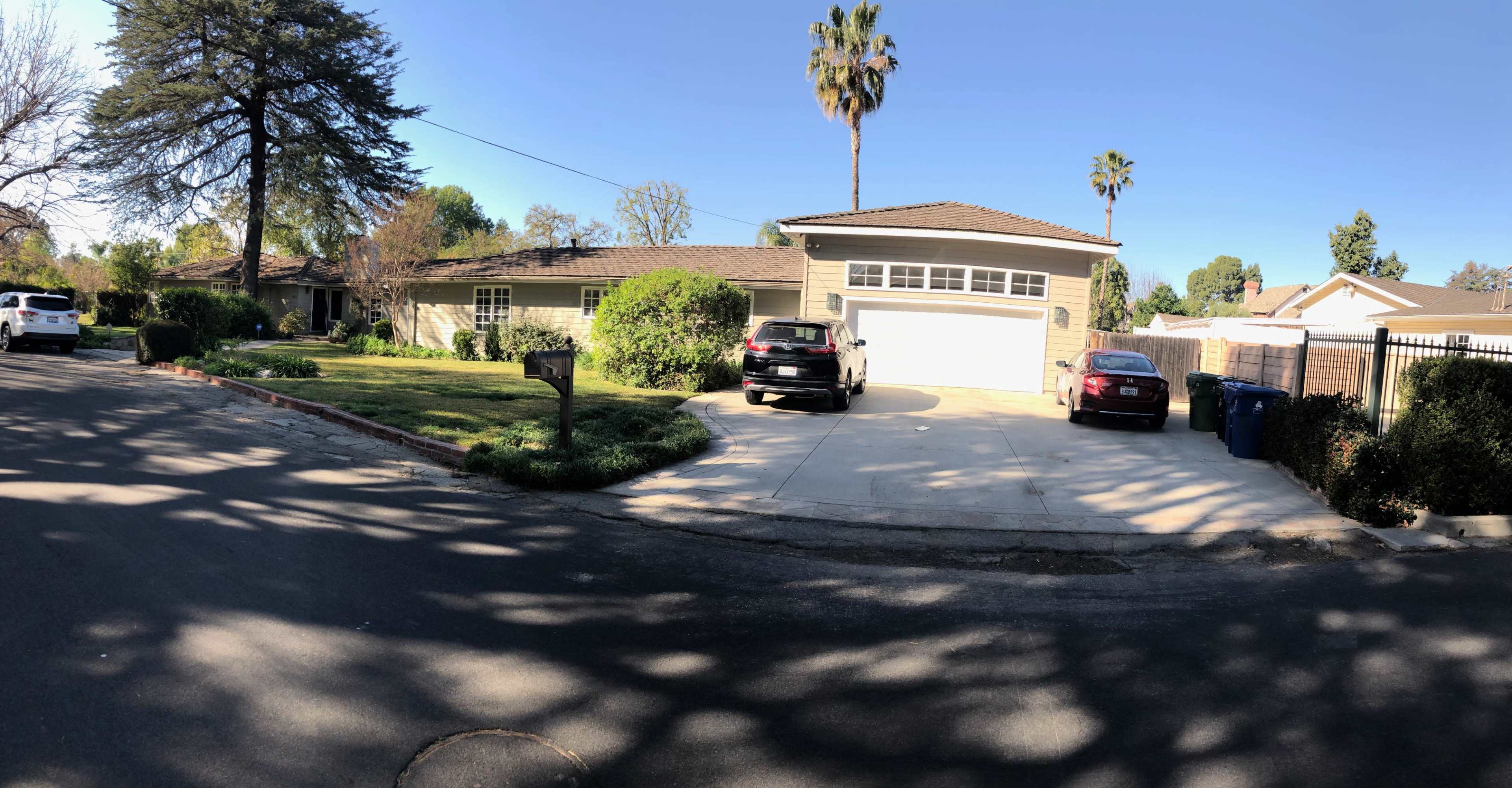 A residential house with a two-car garage and a neatly landscaped front yard, located on a quiet street with parked vehicles.