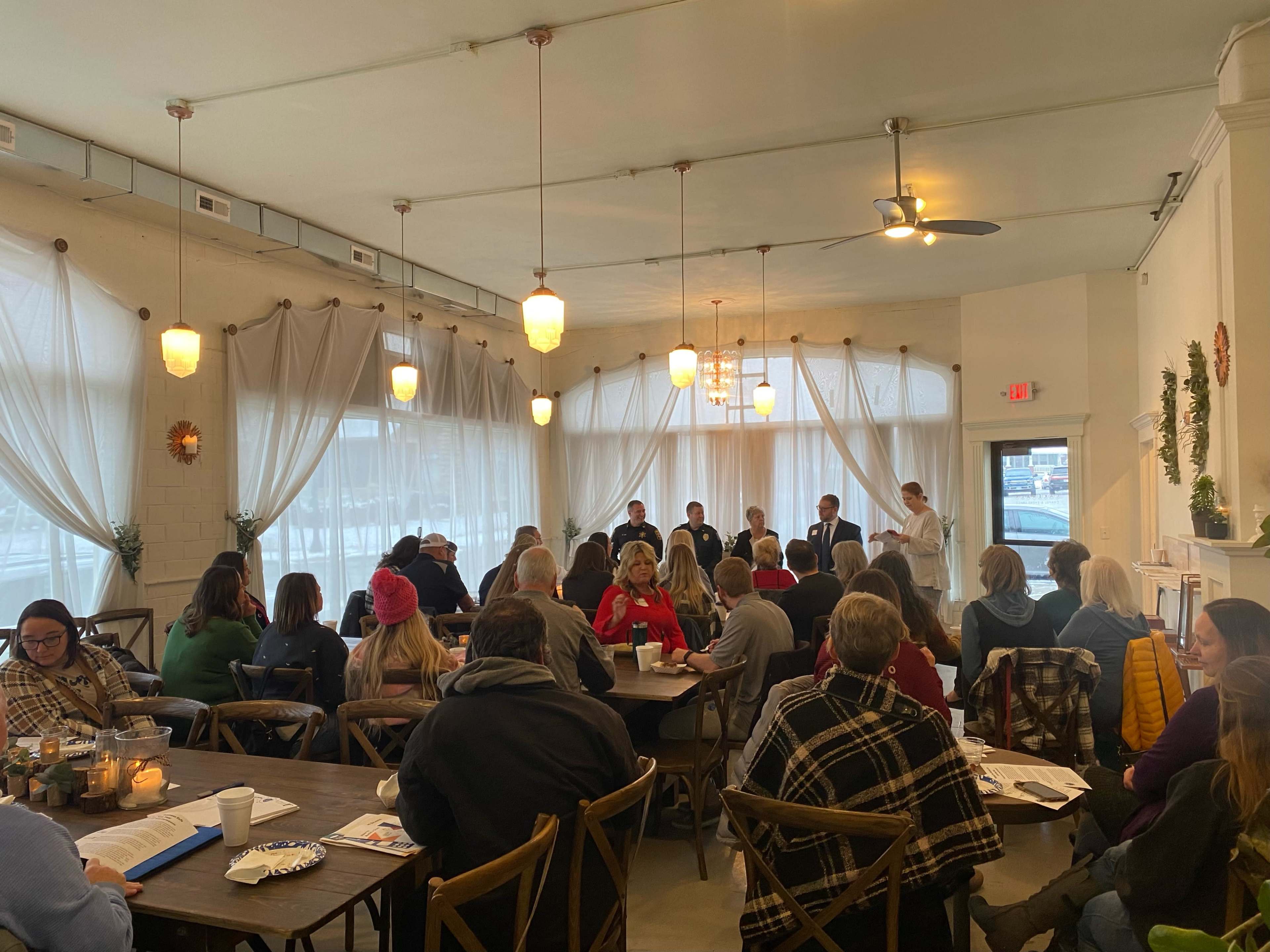 A group of people is seated in a cafe, attentively listening to a panel discussion at the front of the room.