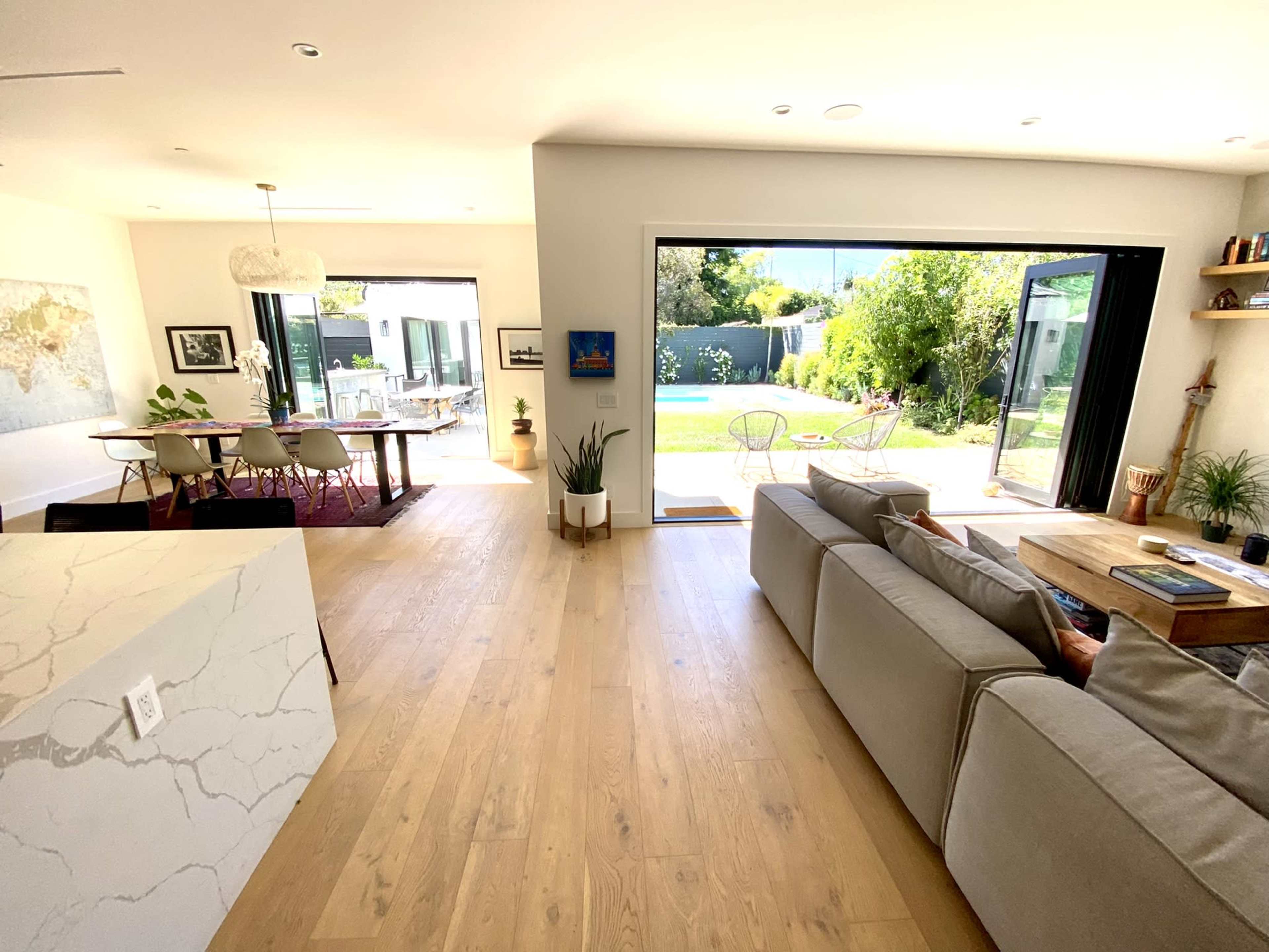A modern living space with an open layout, featuring a light-filled room connected to a patio and a pool area visible through large sliding glass doors.