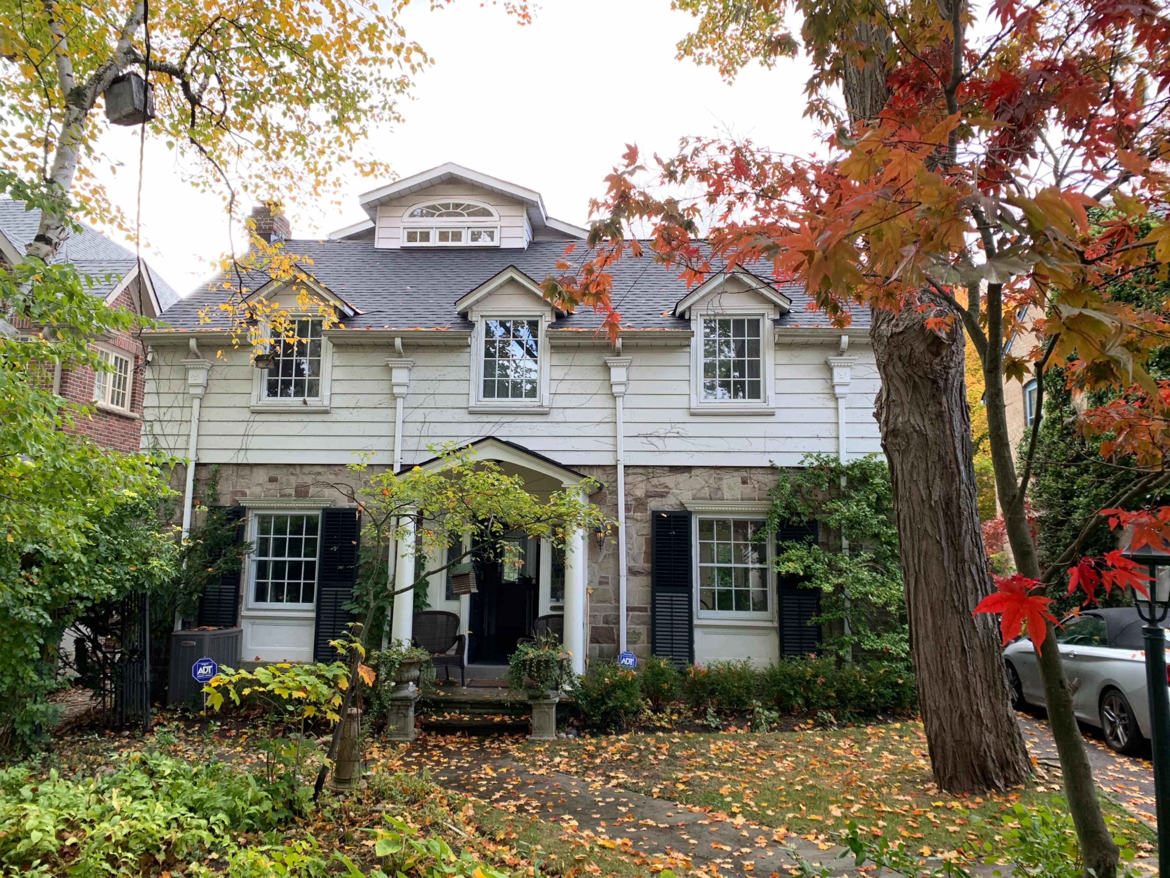 A two-story house with a stone and wooden exterior, surrounded by fall foliage and a well-maintained garden.