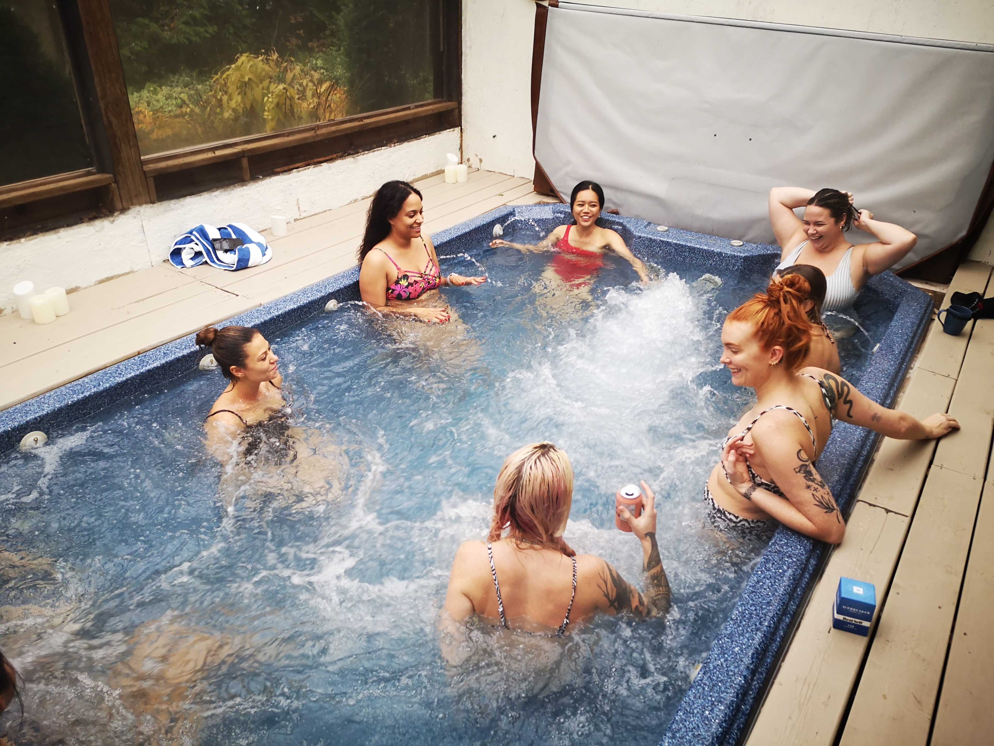 A group of seven women is enjoying time together in a hot tub, creating splashes of water.