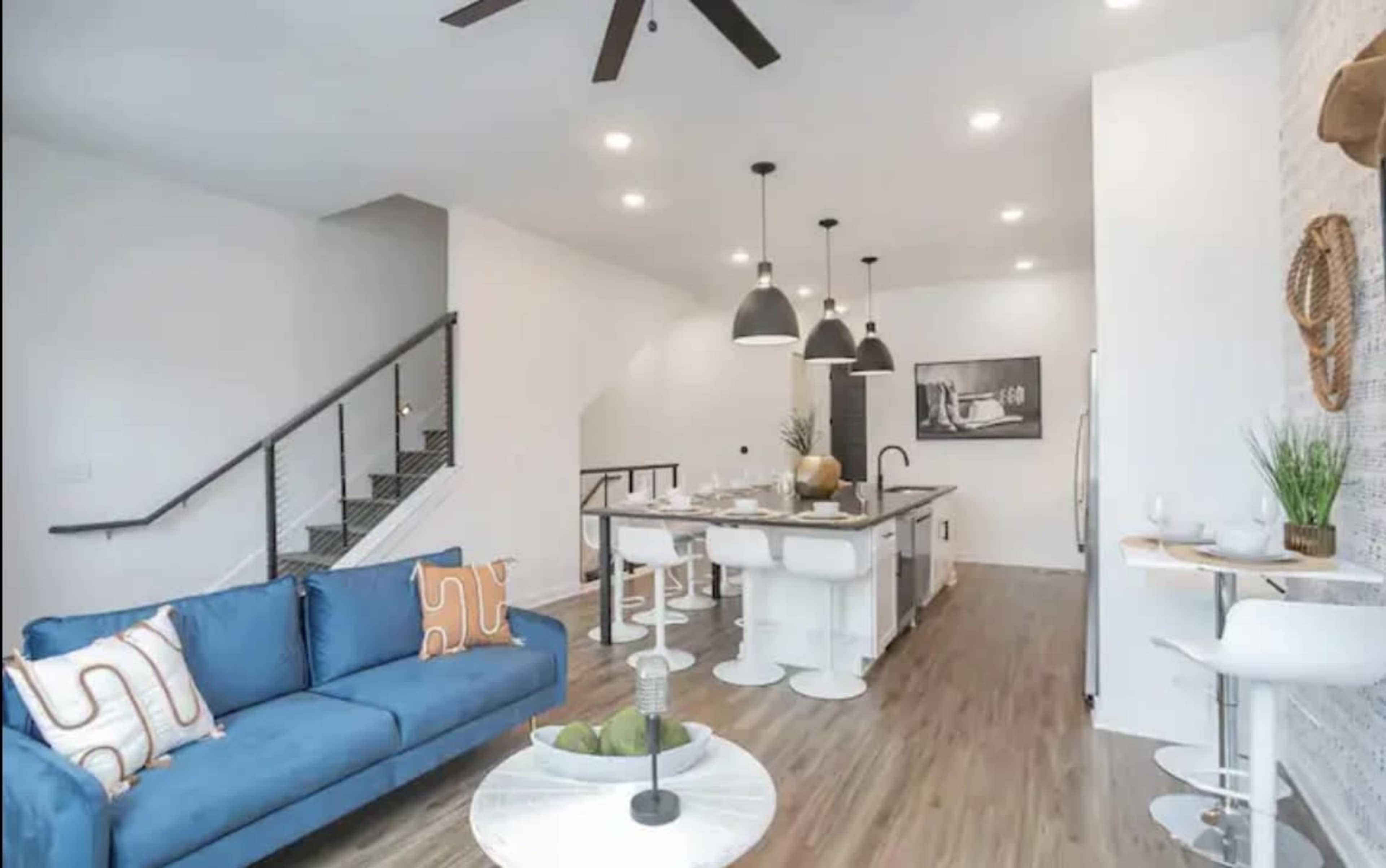A modern living space with a blue sofa, circular coffee table, and a kitchen area featuring a large island and pendant lighting.