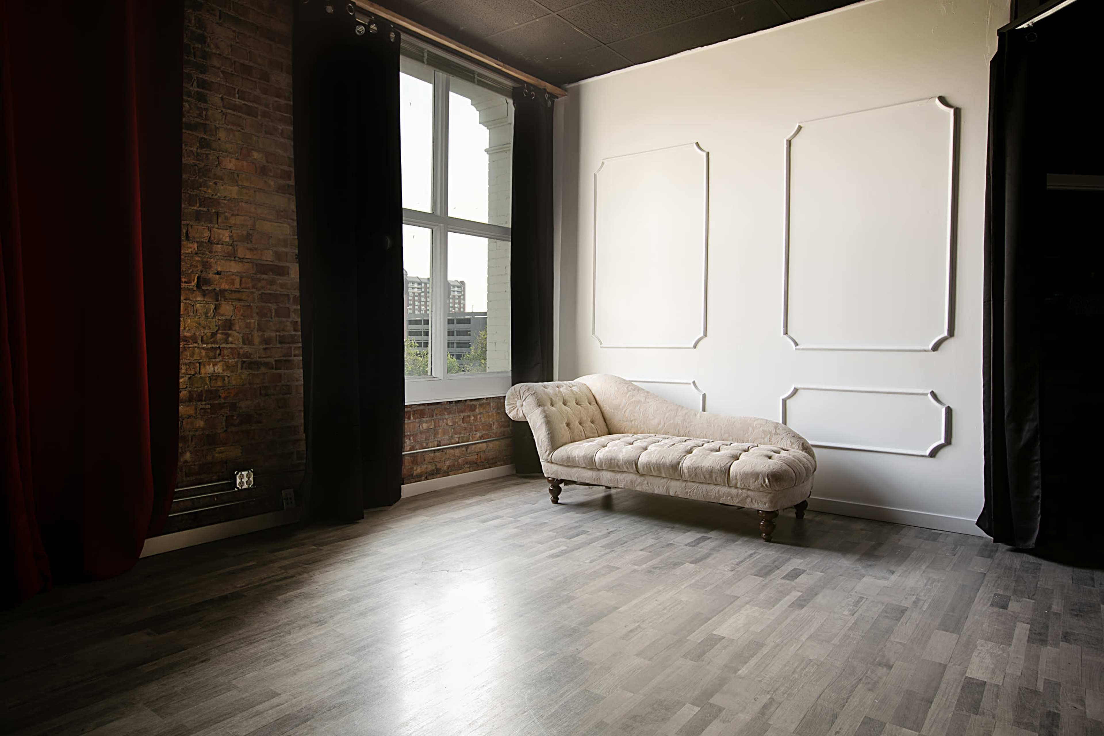 A spacious interior with a tufted chaise lounge against a wall with decorative panels and large windows letting in natural light.