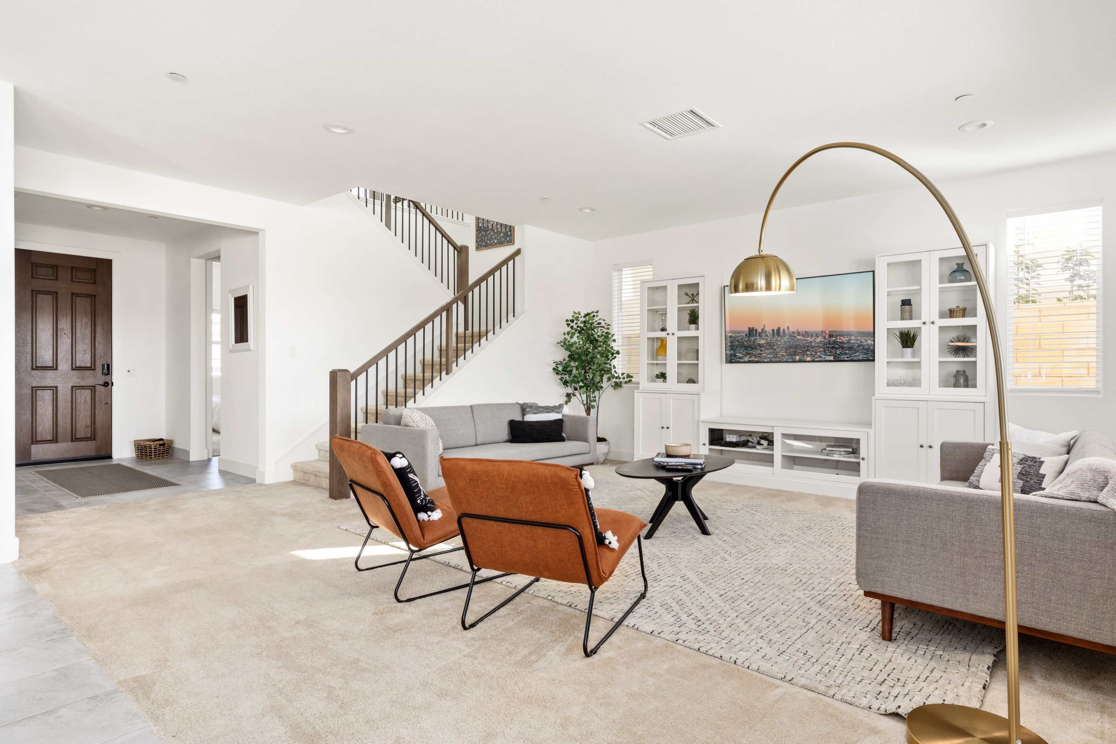 A modern living room featuring a staircase, two chairs, a coffee table, and built-in shelves with a TV.