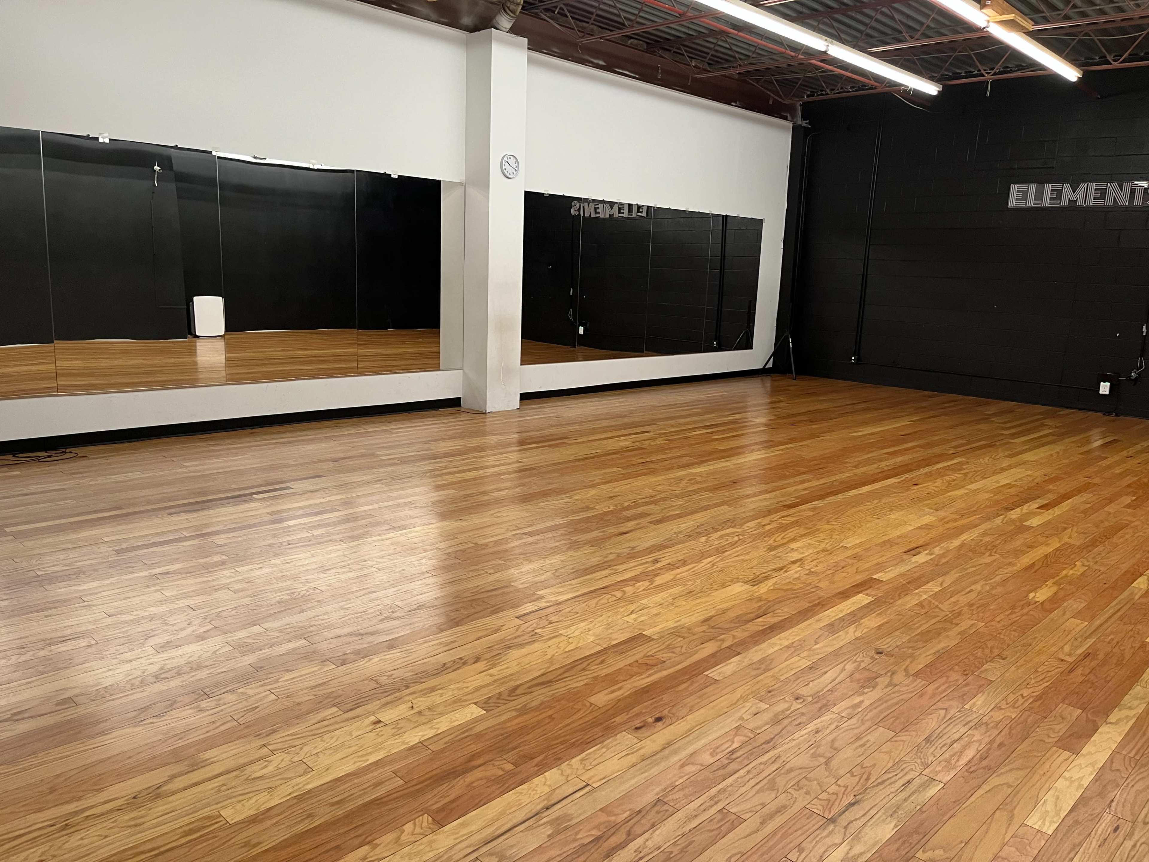 An empty dance studio with wooden flooring and a large mirrored wall.